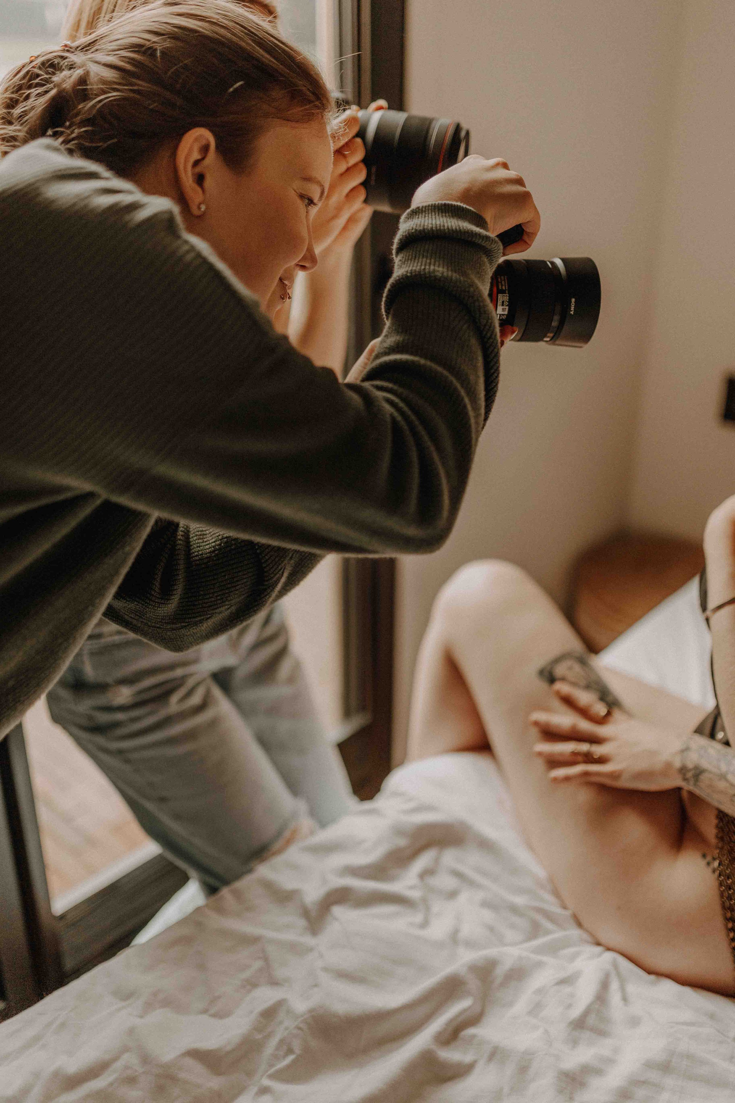 Eine Frau fotografiert eine nackte Person liegend auf einem Bett.