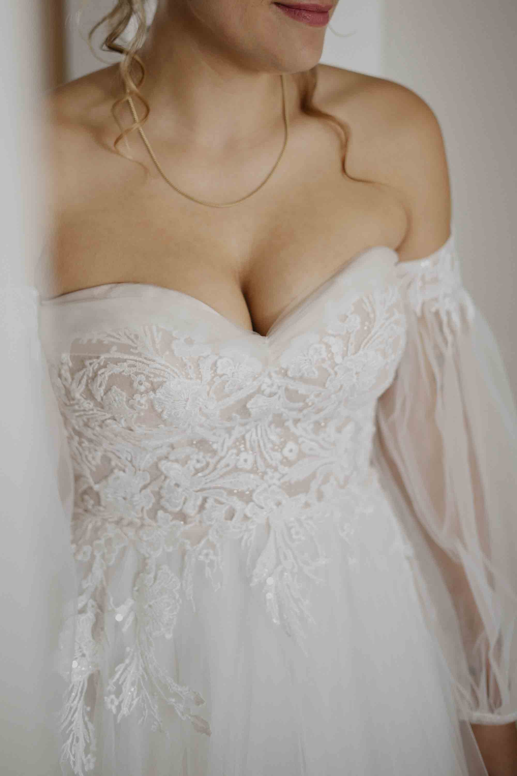 Nahaufnahme eines Hochzeitskleides mit floralen Stickereien an der Brust und transparenten Ärmeln.