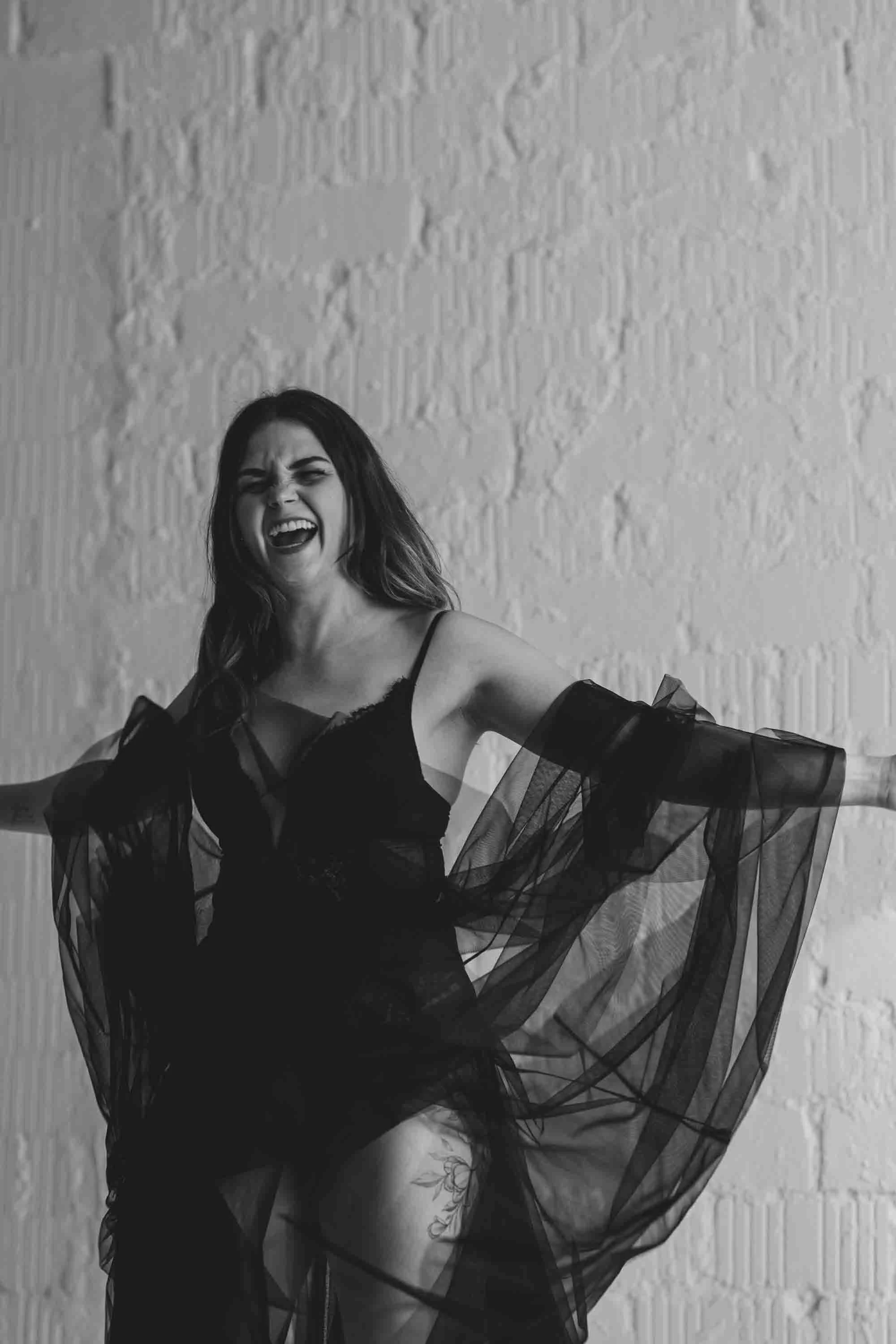 Schwarze und weiße Fotos einer lachenden Frau in einem schwarzen, transparenten Kleid vor einer weißen Wand.