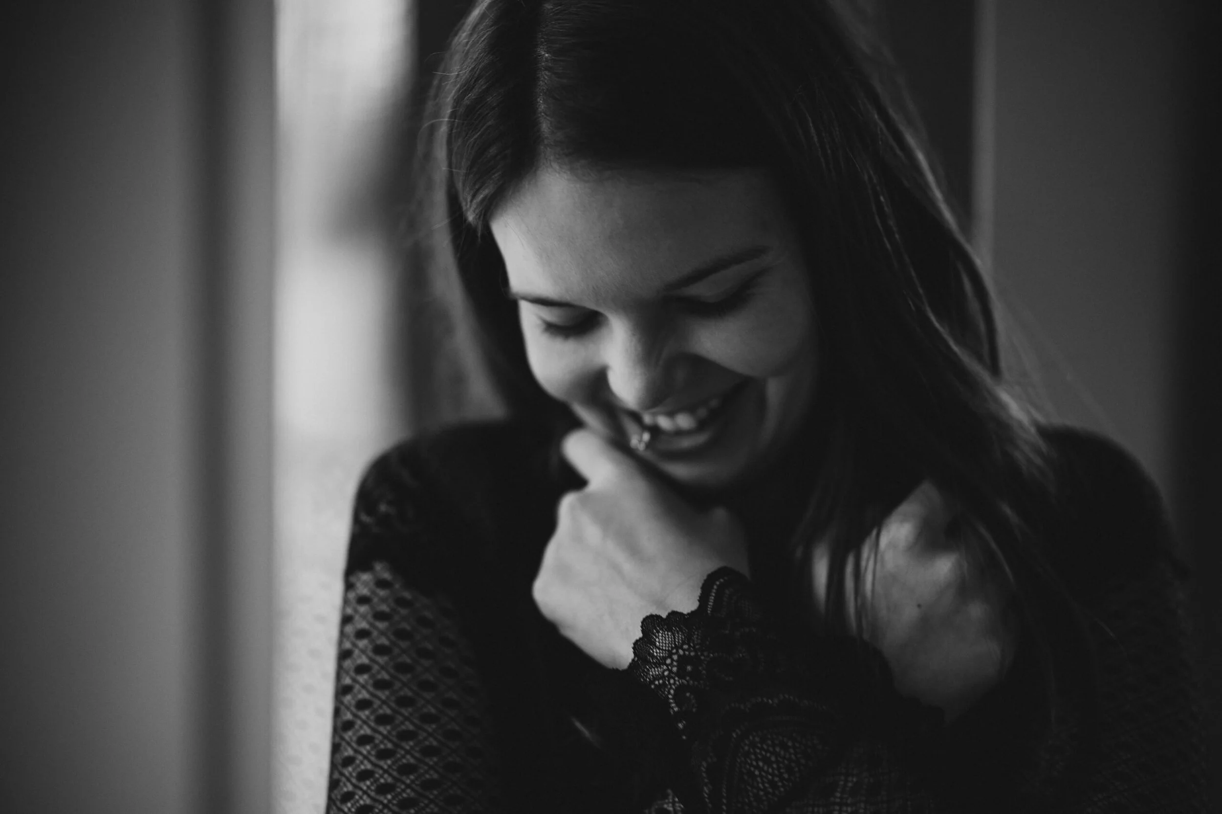 Lächelnde junge Frau mit schwarzen Haaren, die sich die Schulter hält, in Schwarz-Weiß-Foto.