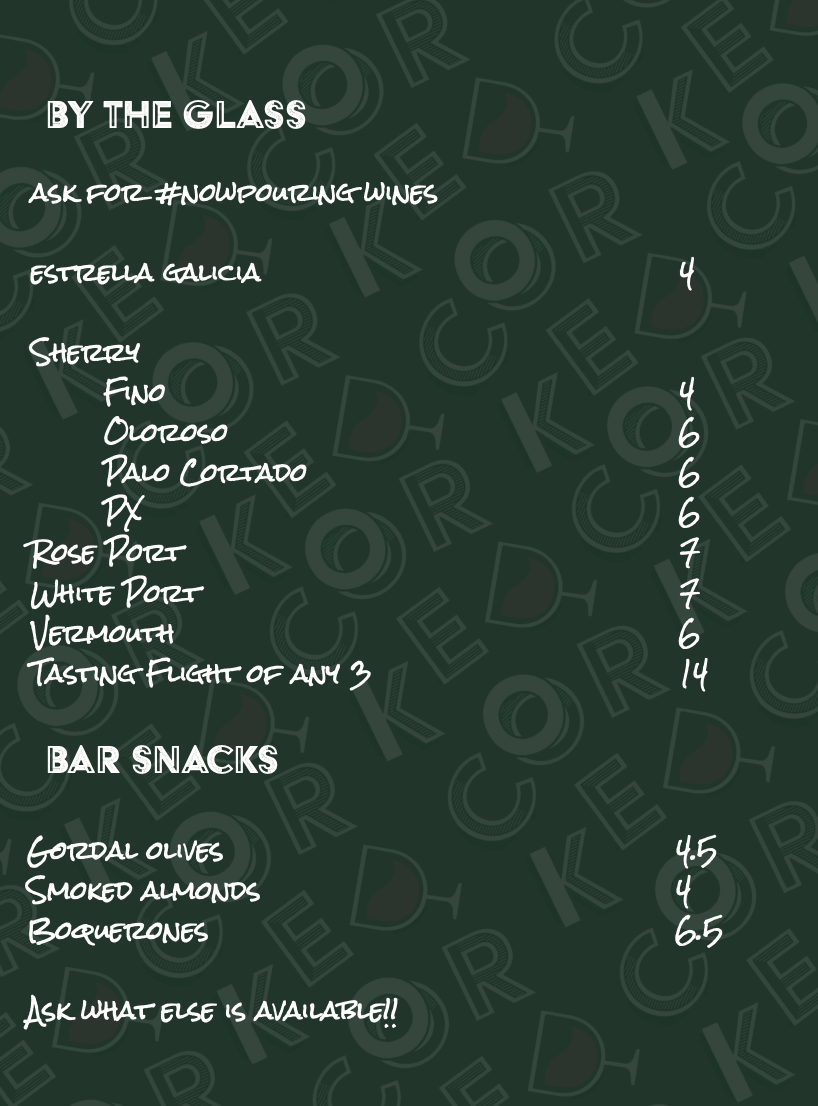 Menu board with wine and bar snack options written on a dark green background with a pattern of playing card symbols.