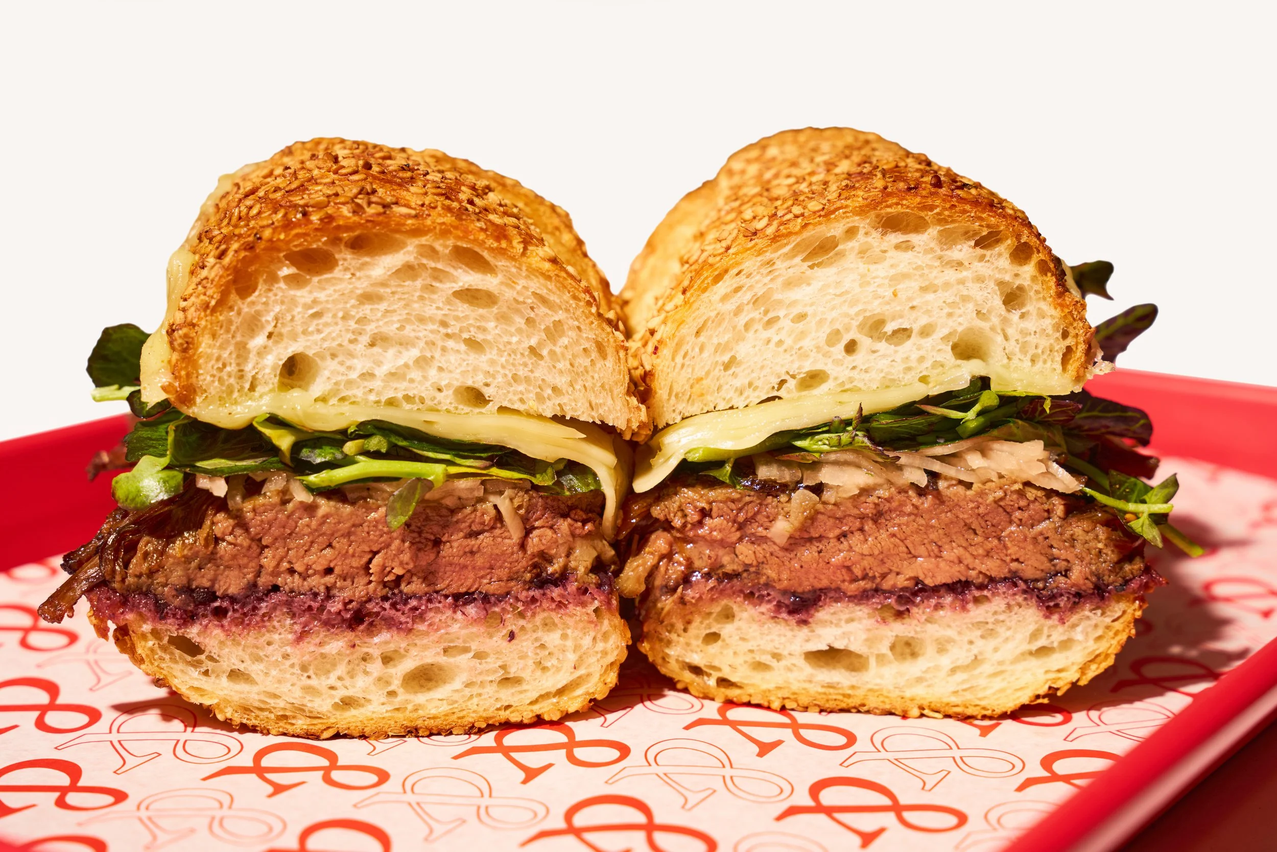 Close-up of a porchetta sandwich cross section, on a red tray lined with patterned ampersand paper.