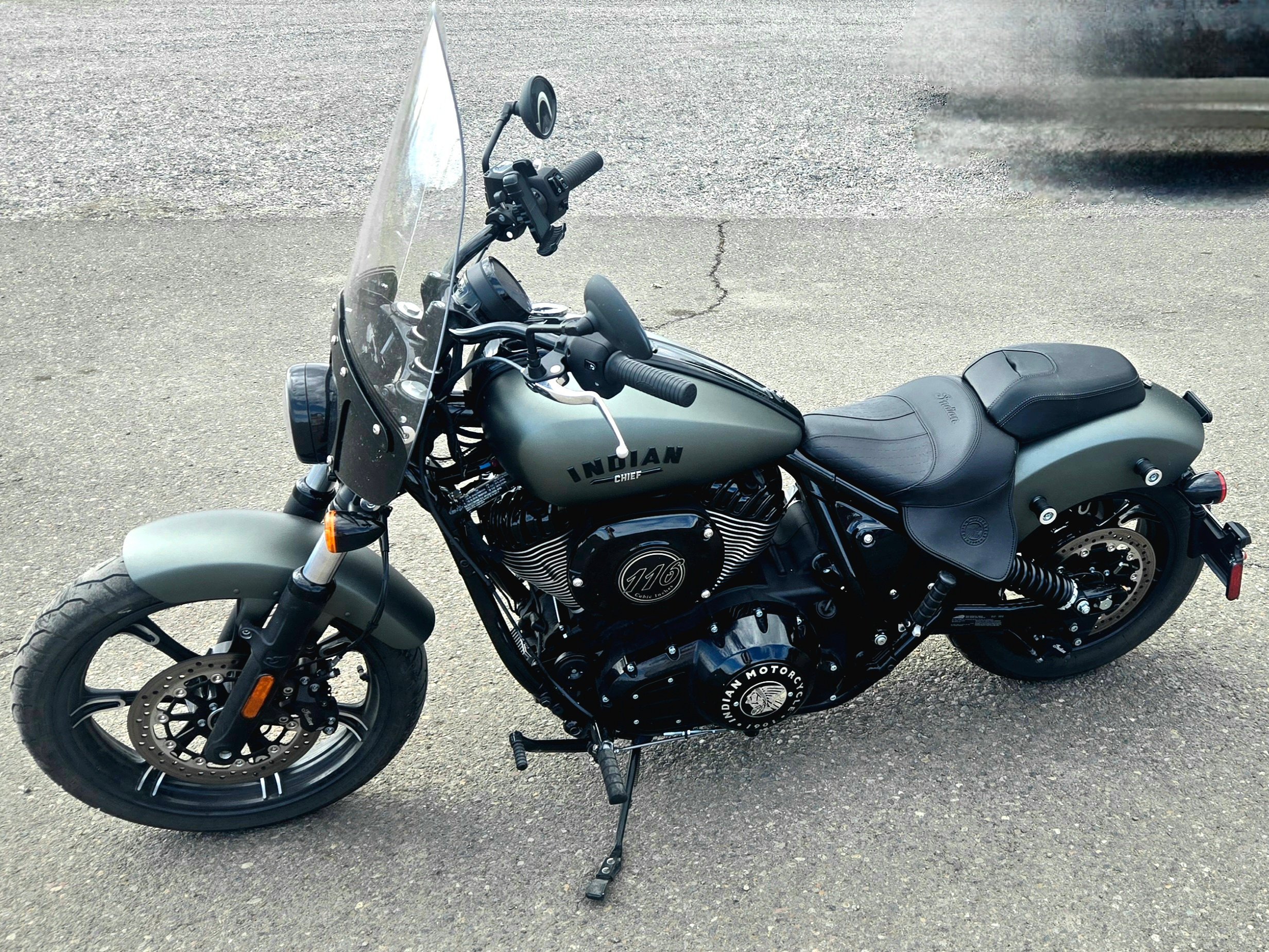 A matte gray Indian Chief motorcycle with black details and a clear windshield parked on a paved surface.