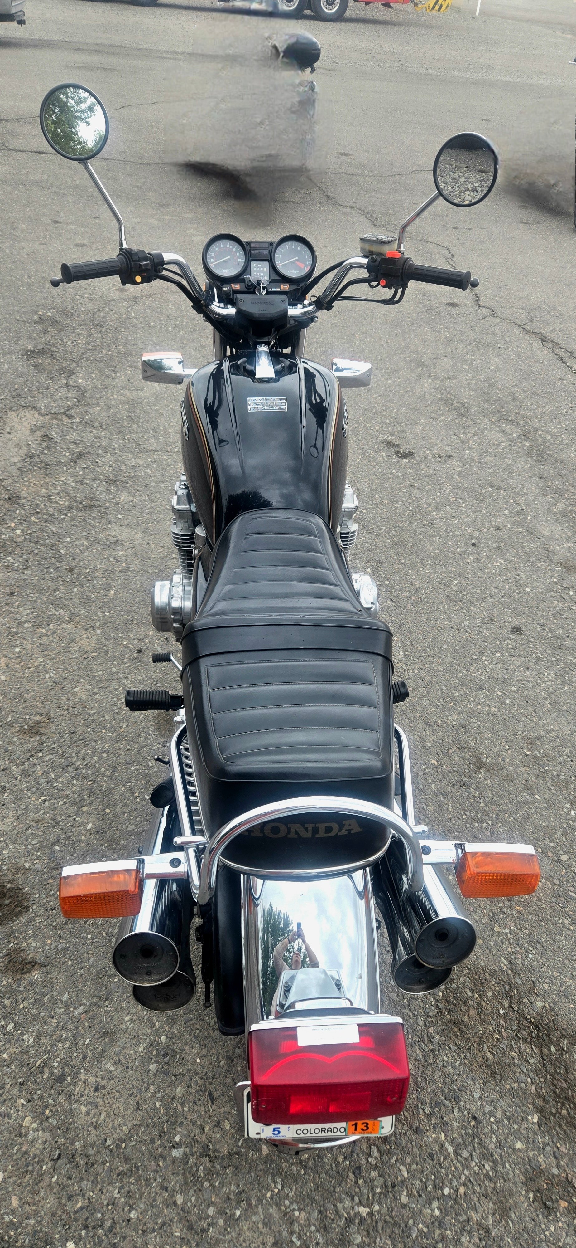Rear view of a black Honda motorcycle parked on a paved surface, with dual exhaust pipes, a black cushioned seat, and a license plate from Colorado.