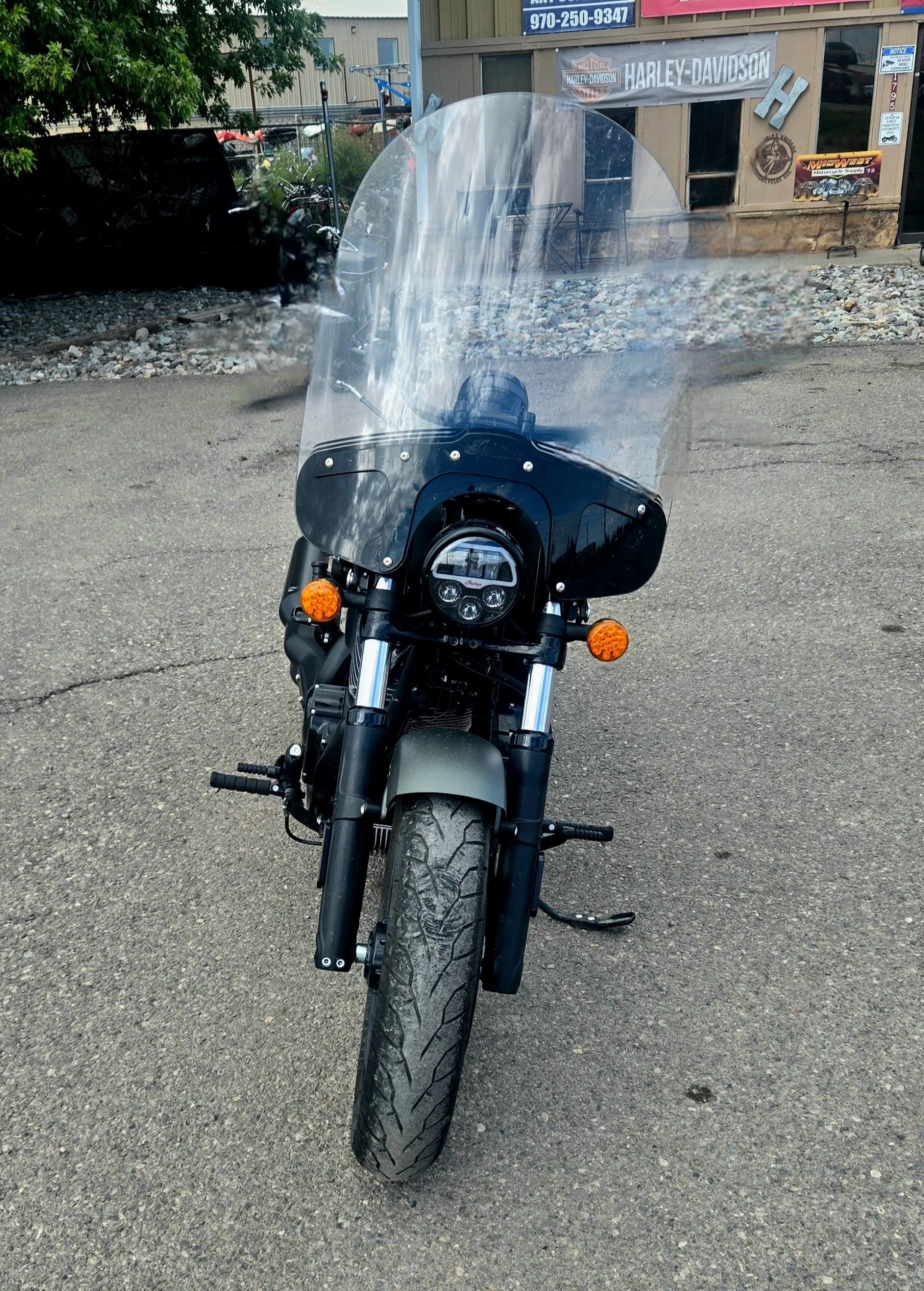 Front view of a black motorcycle with a large windshield parked on asphalt outside a building with Harley-Davidson signage.