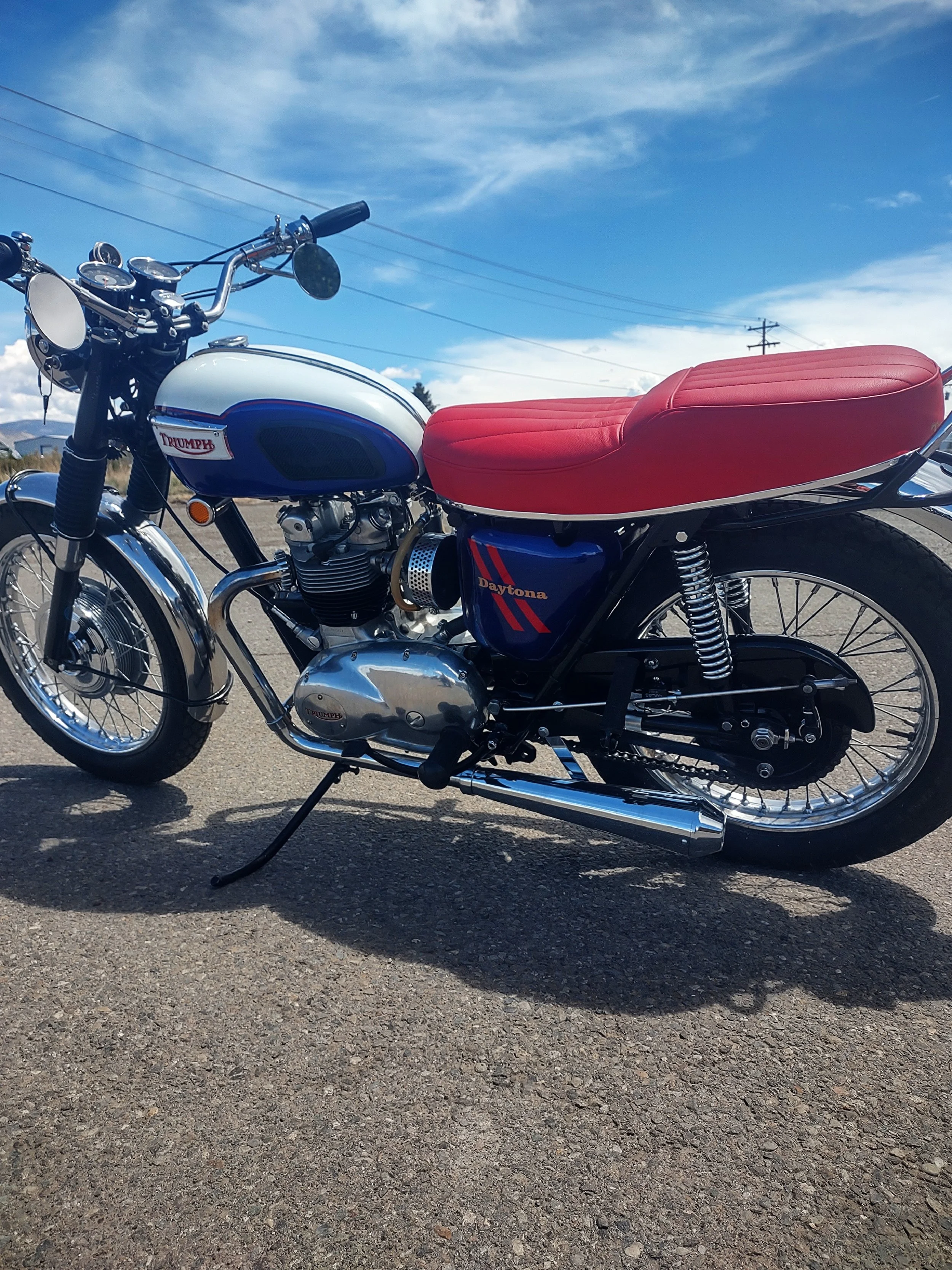 A vintage Triumph Daytona motorcycle parked on a paved road under a partly cloudy sky.