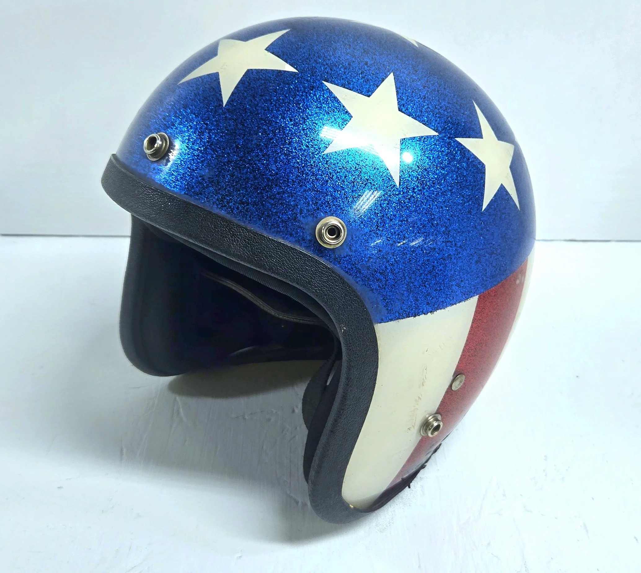 A vintage motorcycle helmet painted with the American flag, featuring white stars on a blue background and red and white stripes.
