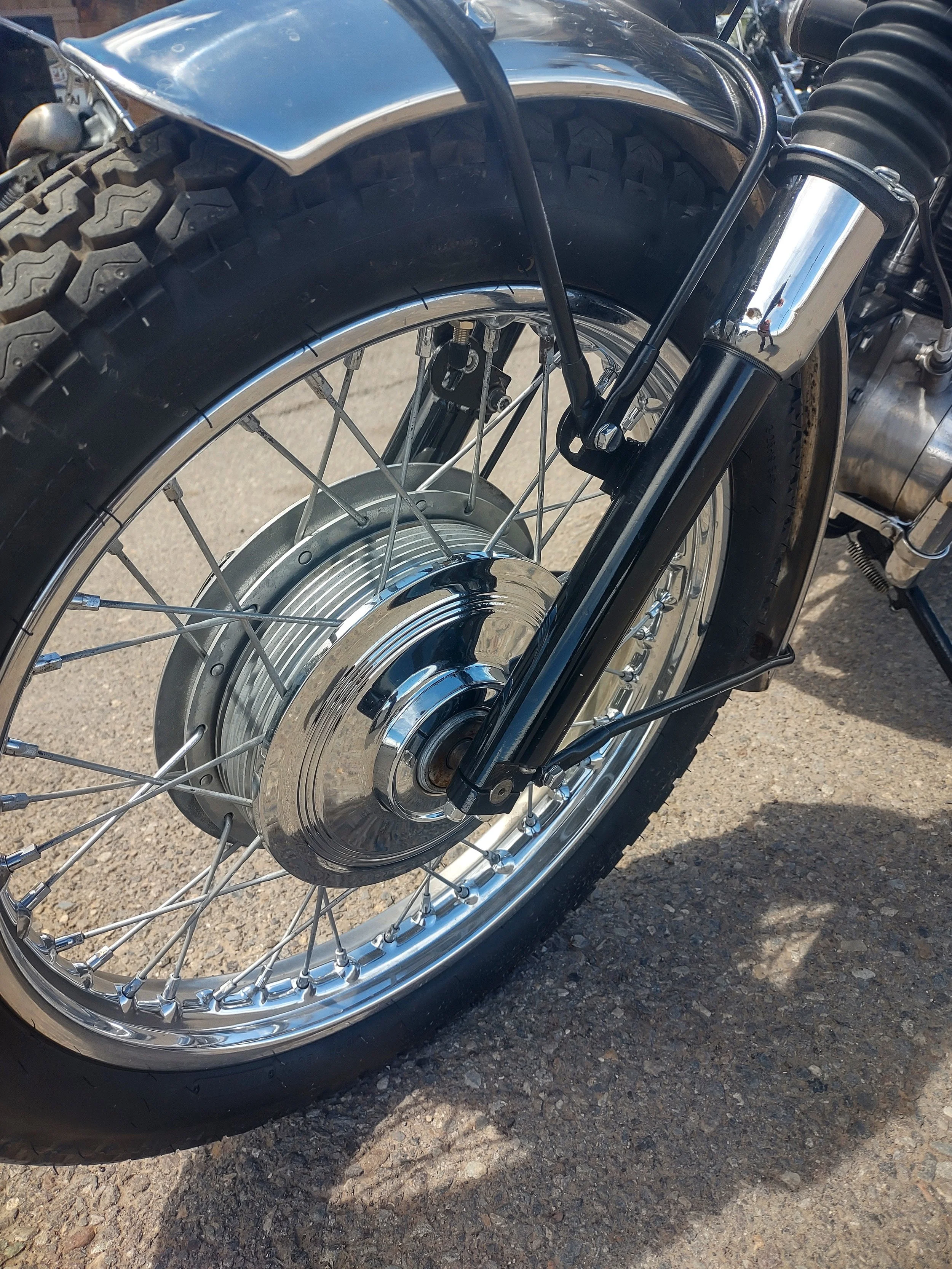 Close-up of a motorcycle front wheel with a black tire, chrome hubcap, and black front fork.