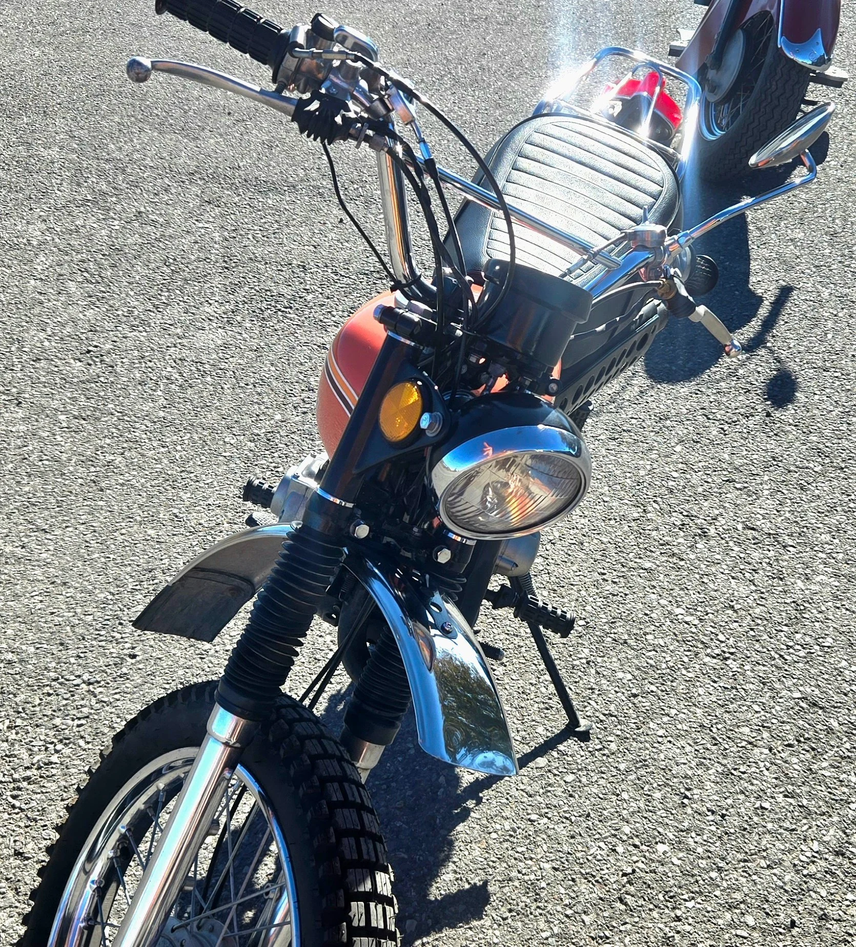 A vintage-style motorcycle with knobby tires, chrome fenders, and a mid-century design, parked on a paved surface.
