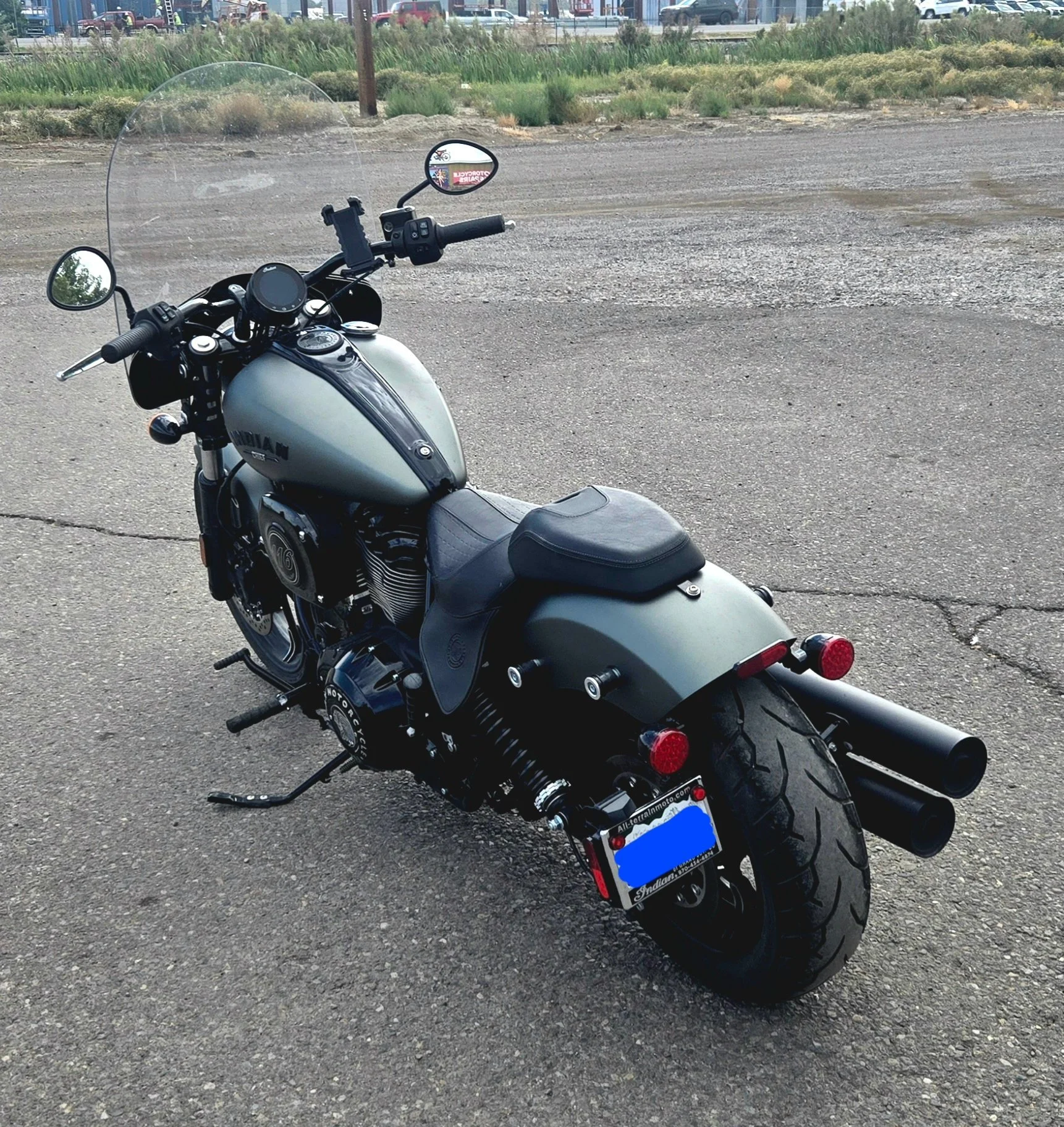 Black and gray Indian motorcycle parked on an asphalt surface with a grassy area and parking lot in the background.