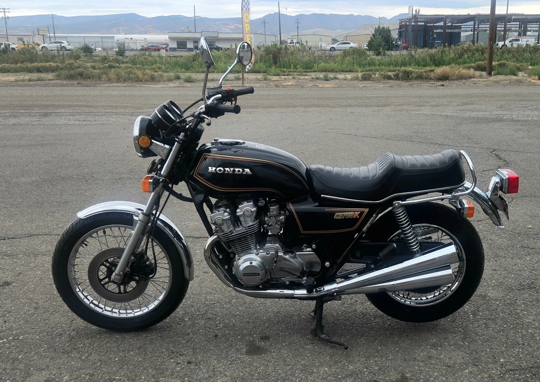 A black vintage Honda motorcycle parked on a paved surface with a scenic mountainous background.
