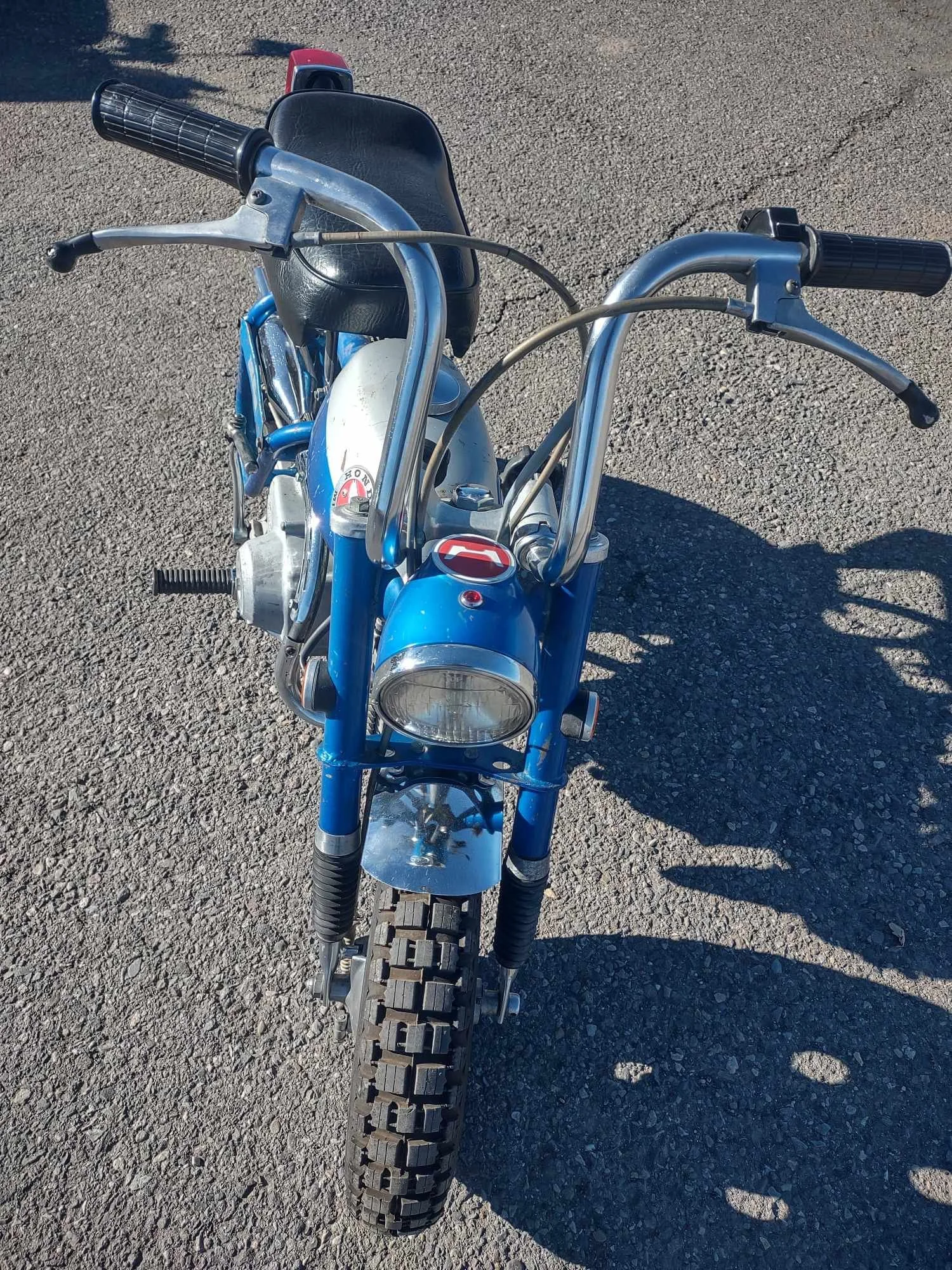 Front view of a vintage blue Honda mini bike with black seat, knobby tires, and chrome handlebars on asphalt.
