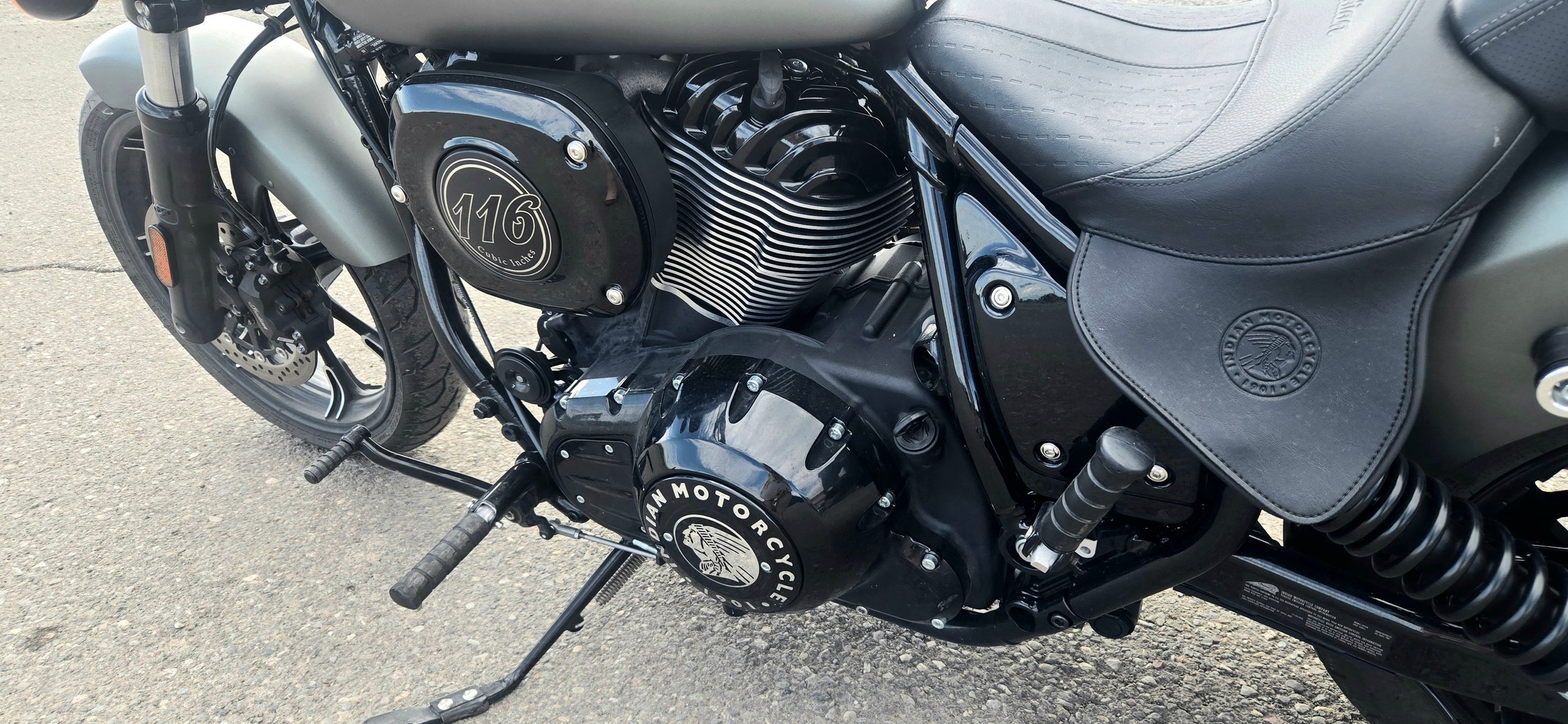 Close-up of a black Indian Motorcycle with a 116 cubic inch engine, showing the engine, part of the frame, front wheel, and a leather seat with the Indian Motorcycle logo.