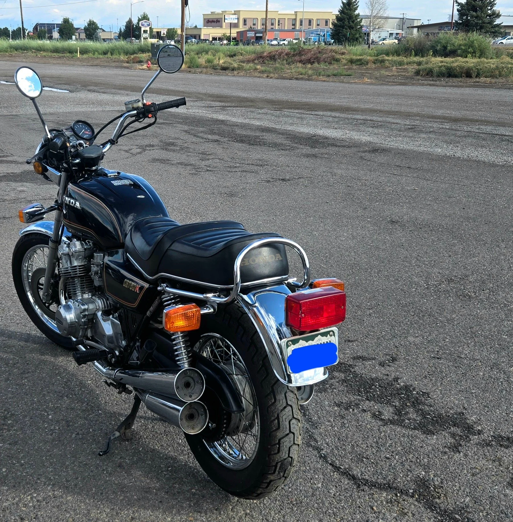A black vintage Honda motorcycle parked on an asphalt lot with a building and trees in the background.