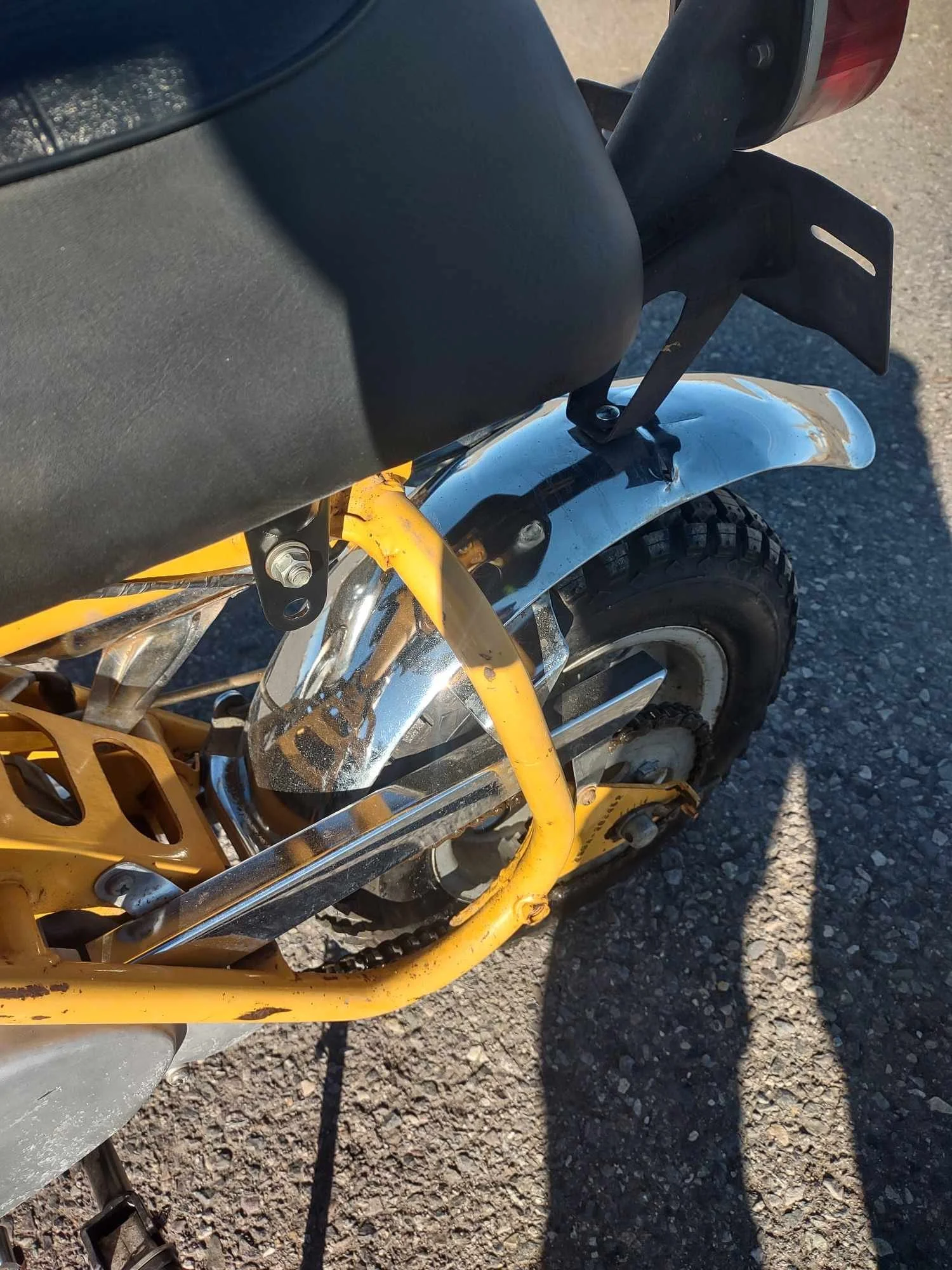 Close-up photo of a yellow and black motorcycle, showing part of the rear wheel, chrome fender, and yellow frame with a black seat and rear light.