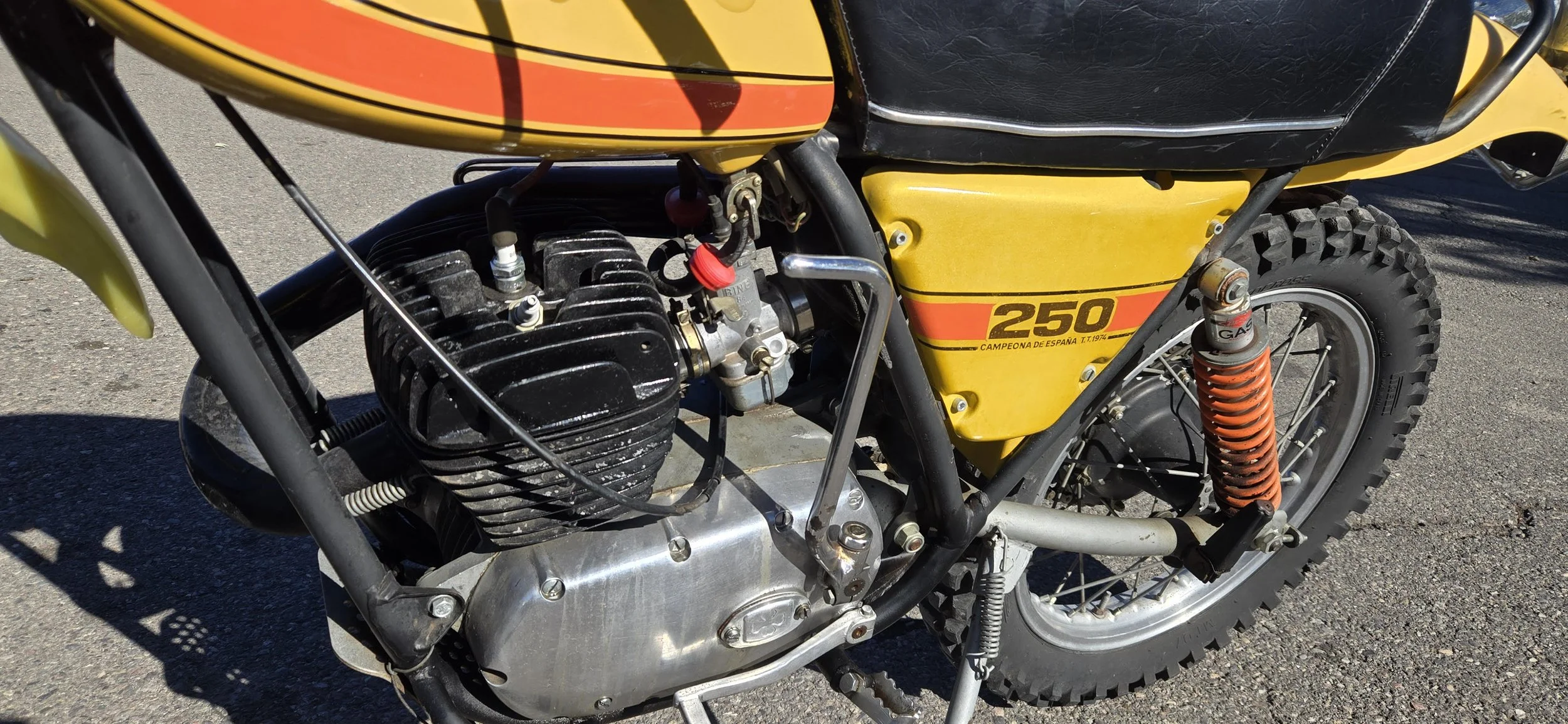 Close-up of a vintage yellow and black off-road motorcycle with a 250cc engine, showing the engine, suspension, tire, and frame details.