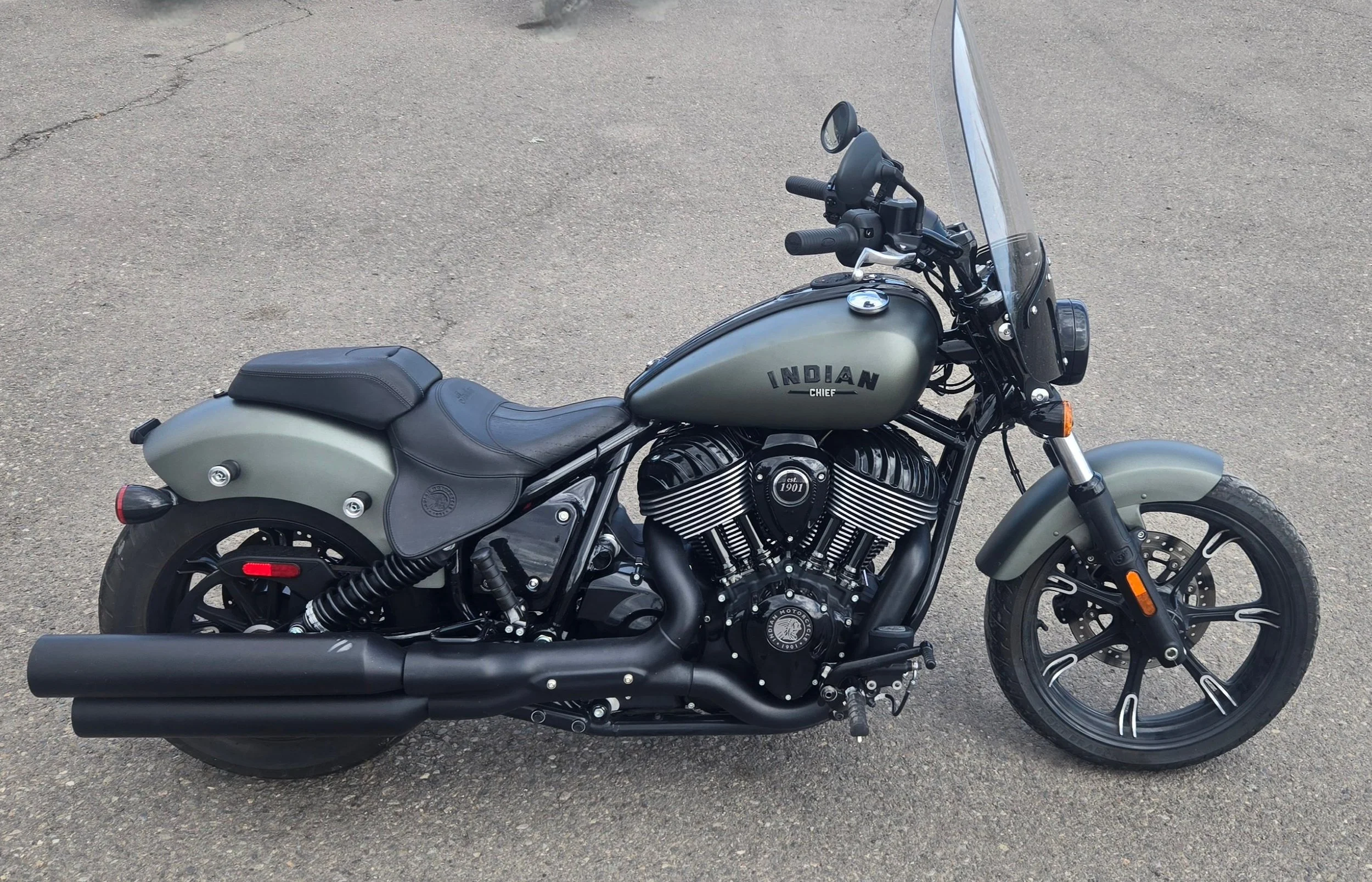 Black and gray Indian Chief motorcycle parked on asphalt, with a large windshield, black exhaust, and black wheels.