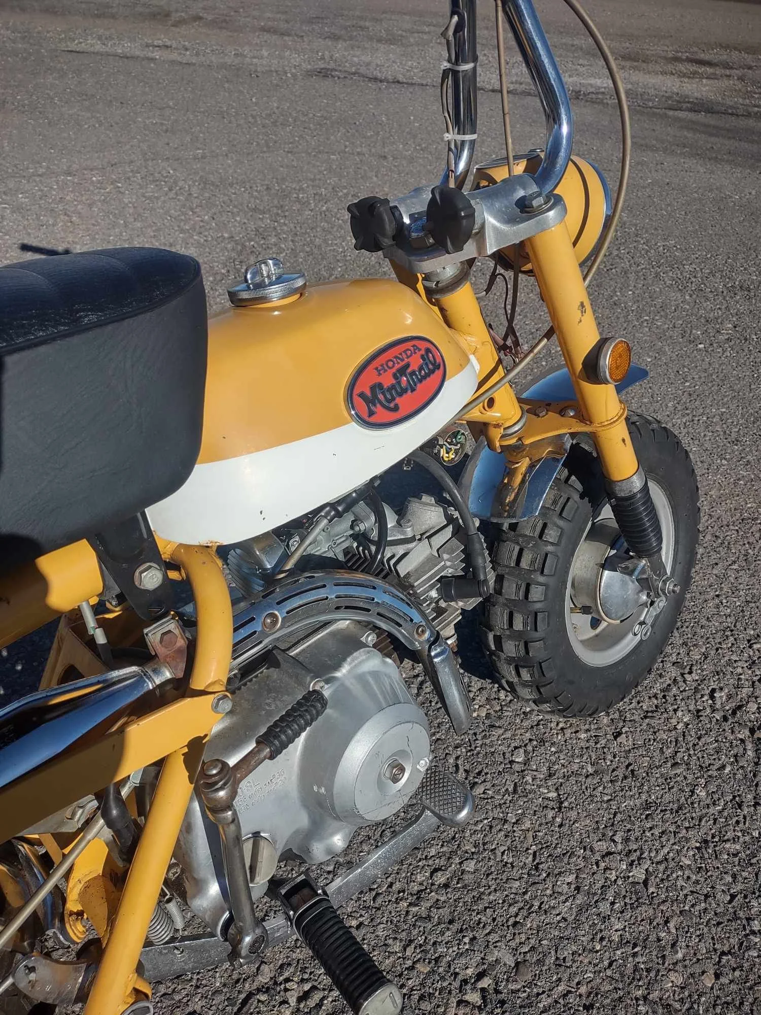 A vintage Honda Monkey motorcycle with a yellow and white fuel tank, black seat, and off-road tires, parked on asphalt.