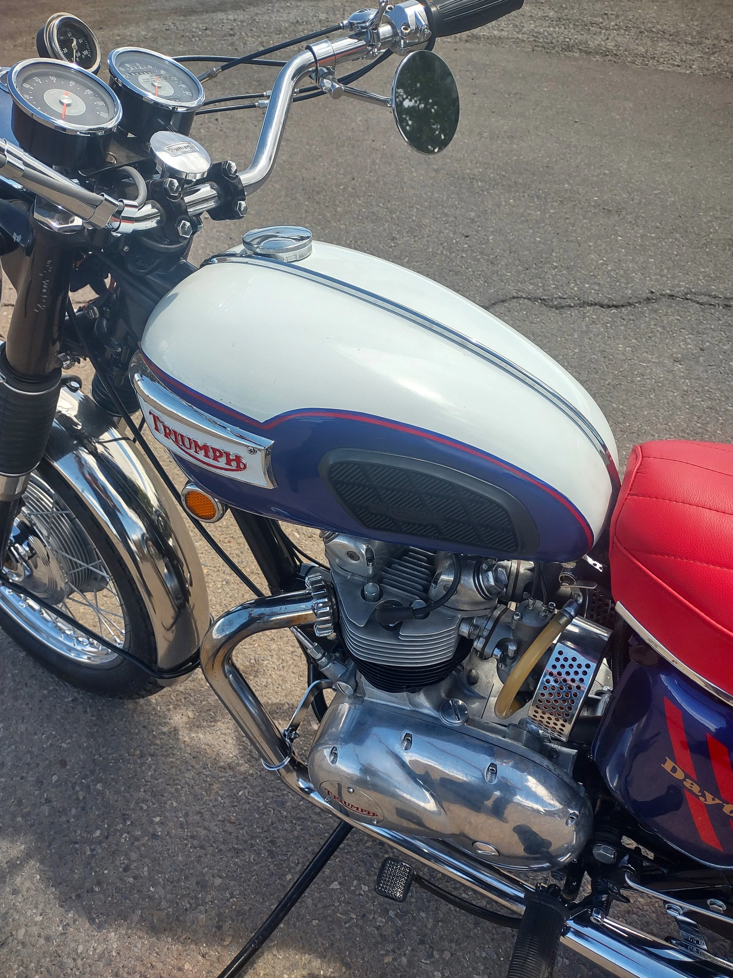 Close-up of a vintage Triumph motorcycle with a white and blue fuel tank, red leather seat, and chrome details.