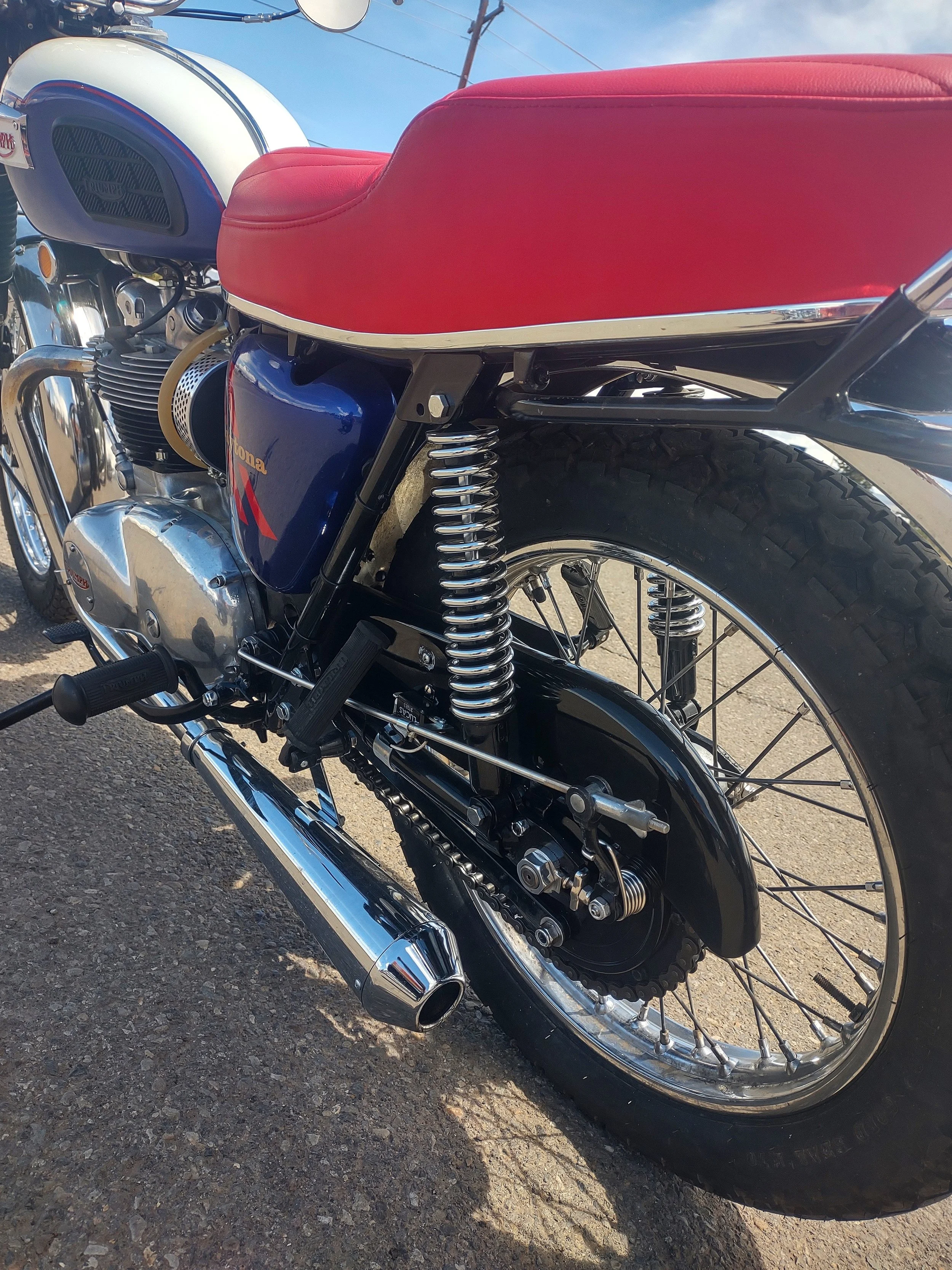 Close-up of a vintage motorcycle with a red seat, black frame, chrome exhaust, and rear suspension.