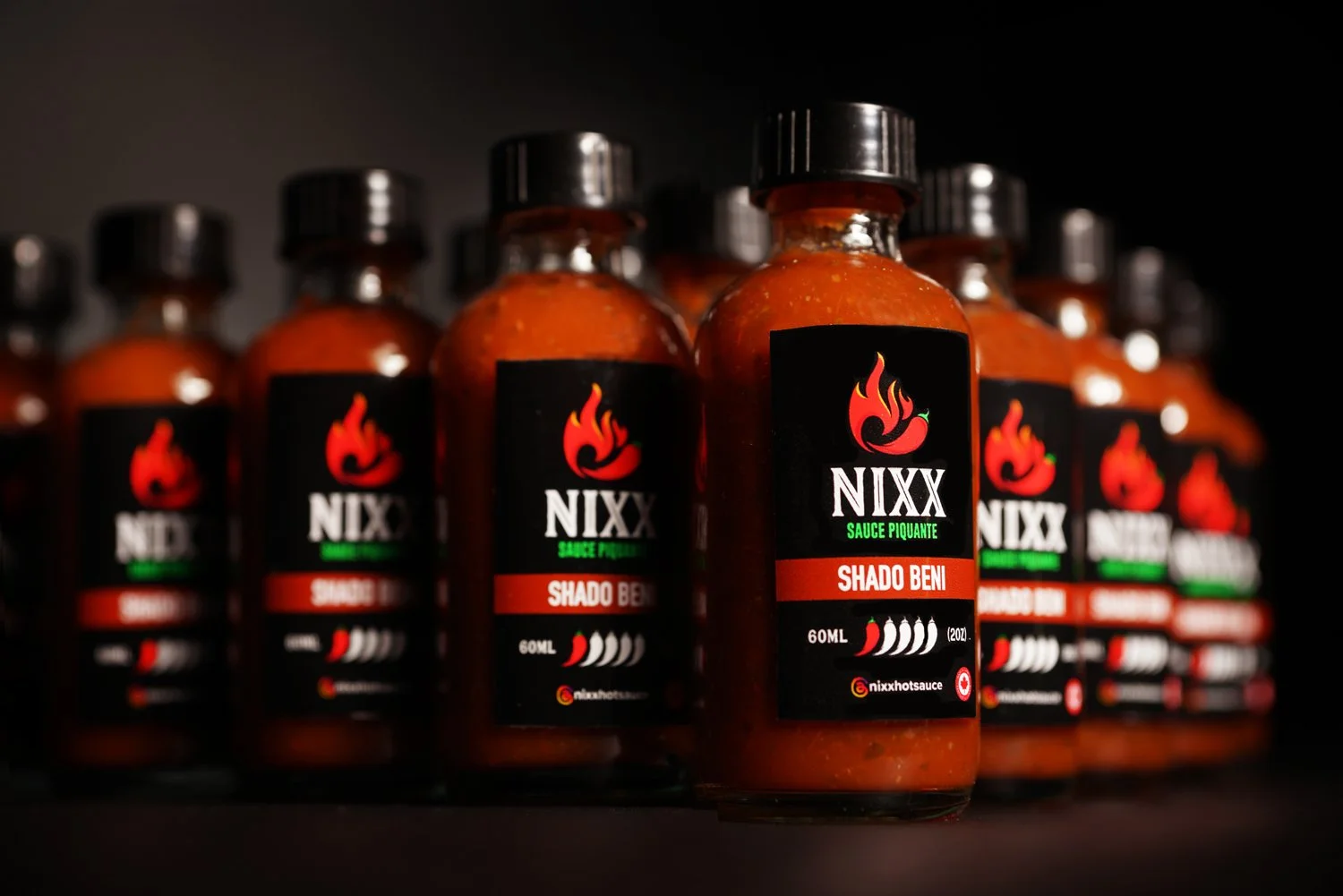 Multiple bottles of NIXX Sriracha-style hot sauce on a dark background.