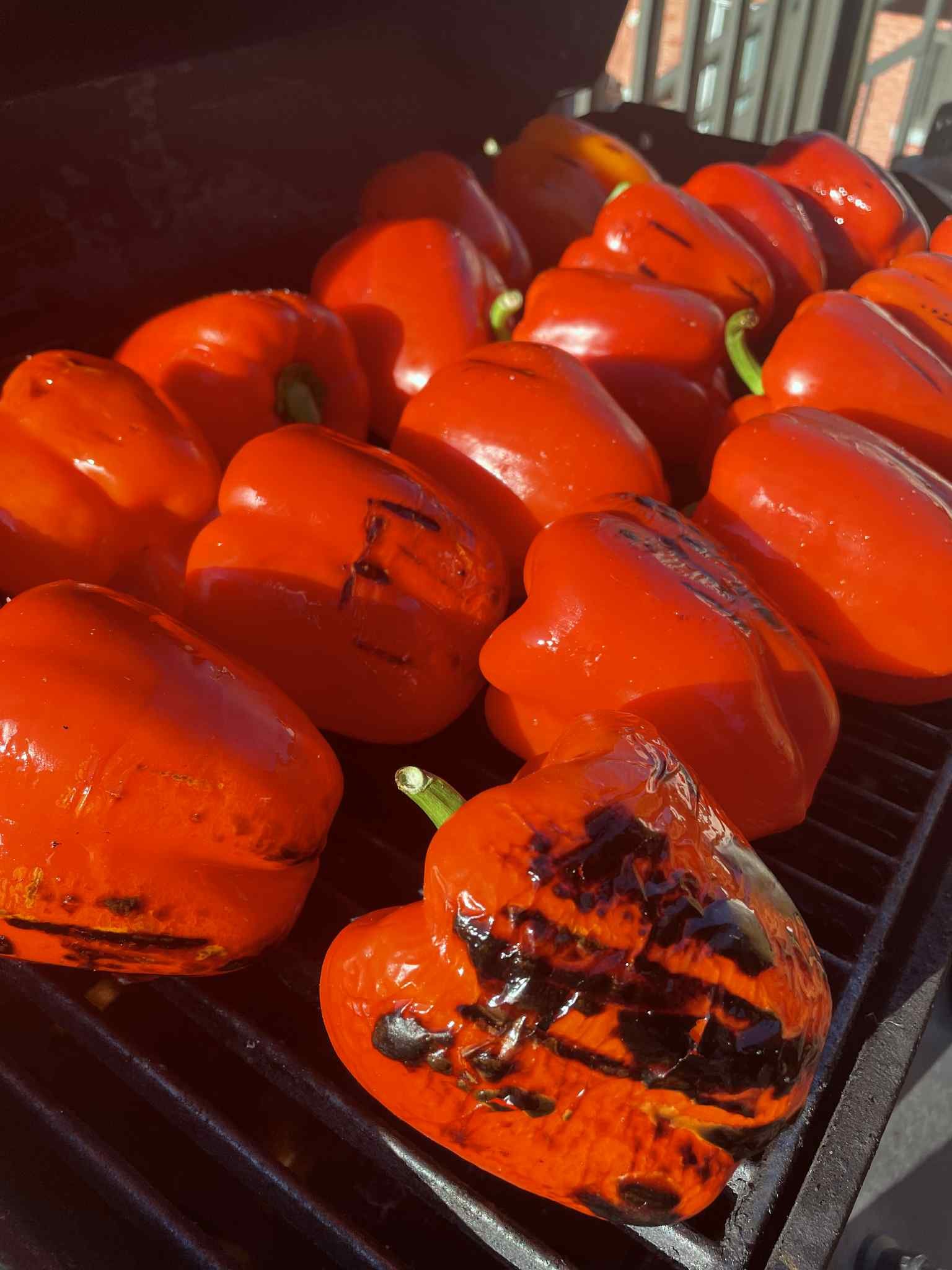 Red bell peppers with charred spots on a grill, some showing grill marks and blackened areas.