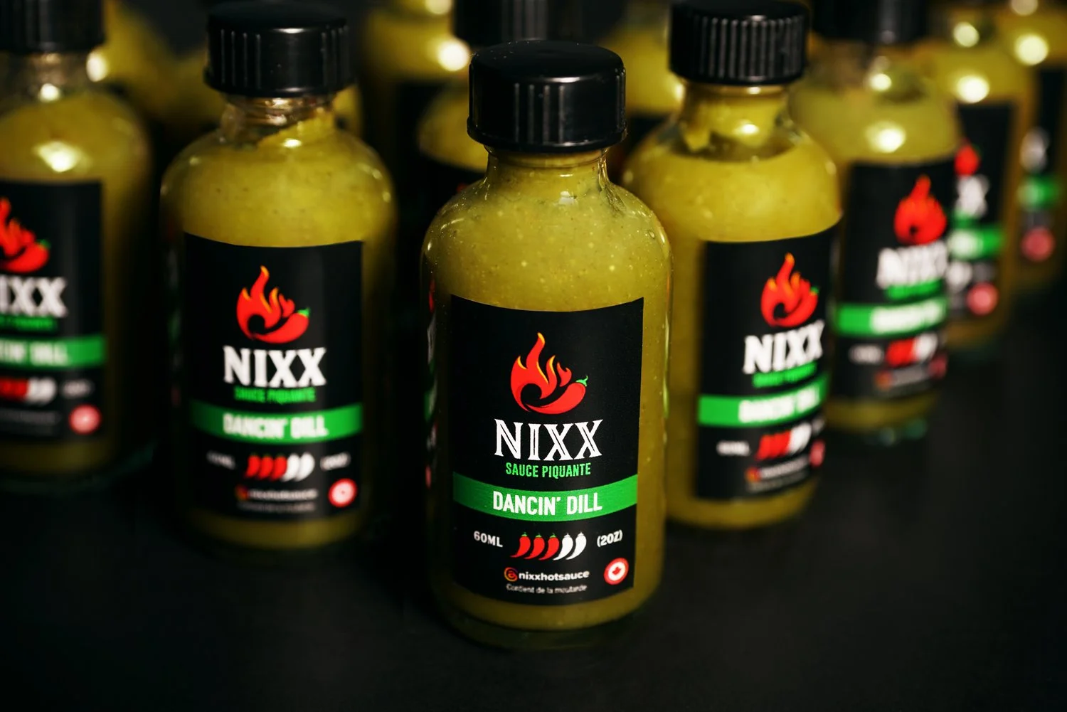 Several bottles of NIXX Sauce Piquante Dancin' Dill hot sauce with black, green, red, and white labels, arranged on a black surface.