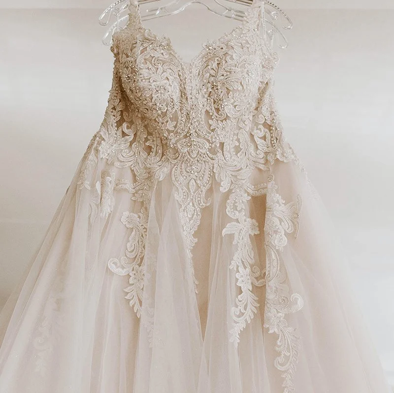 White wedding dress with intricate lace and embroidery on the bodice and skirt, hanging on a clear hanger.