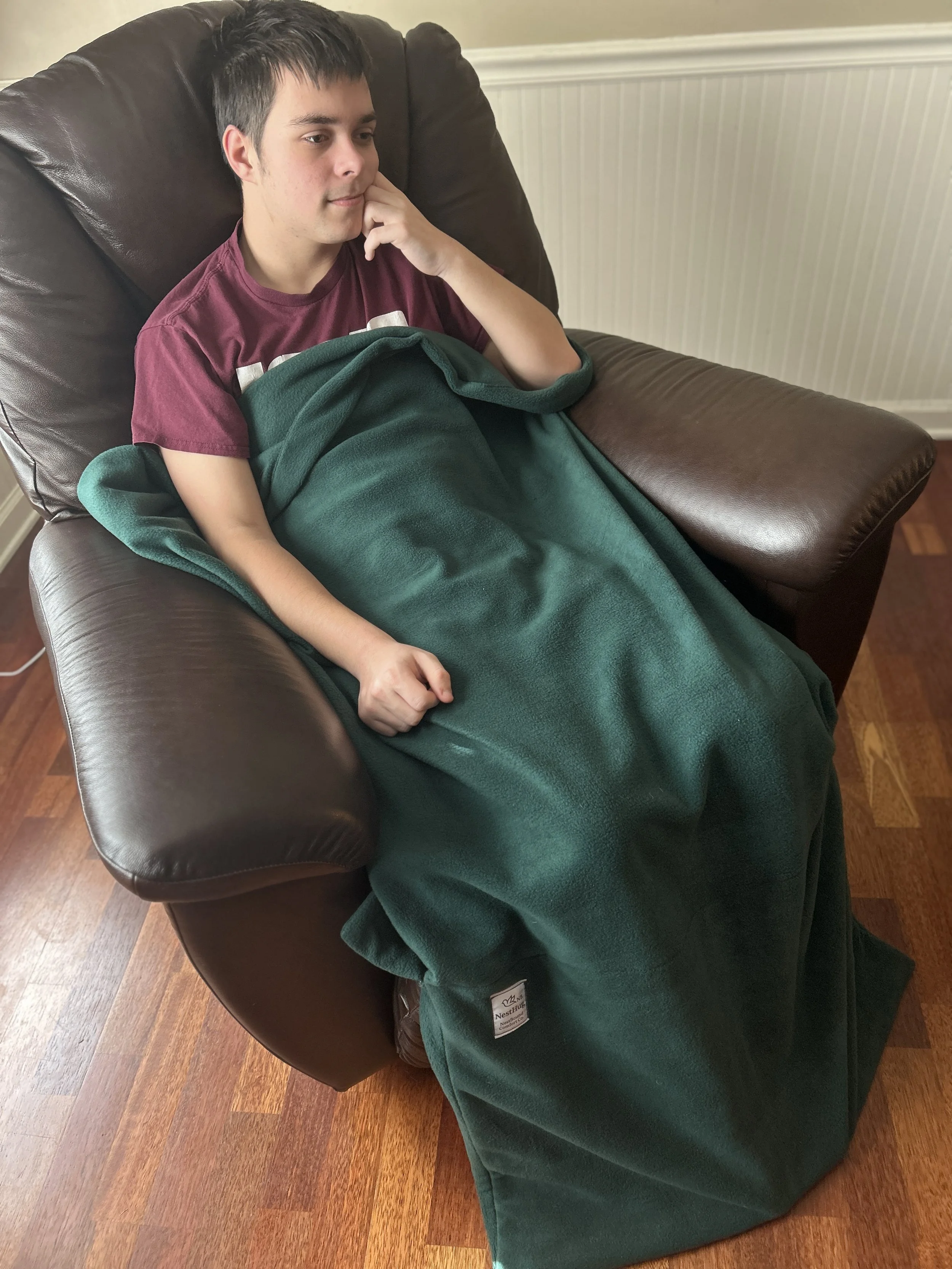 A person sitting, covered by the NestHug blanket.