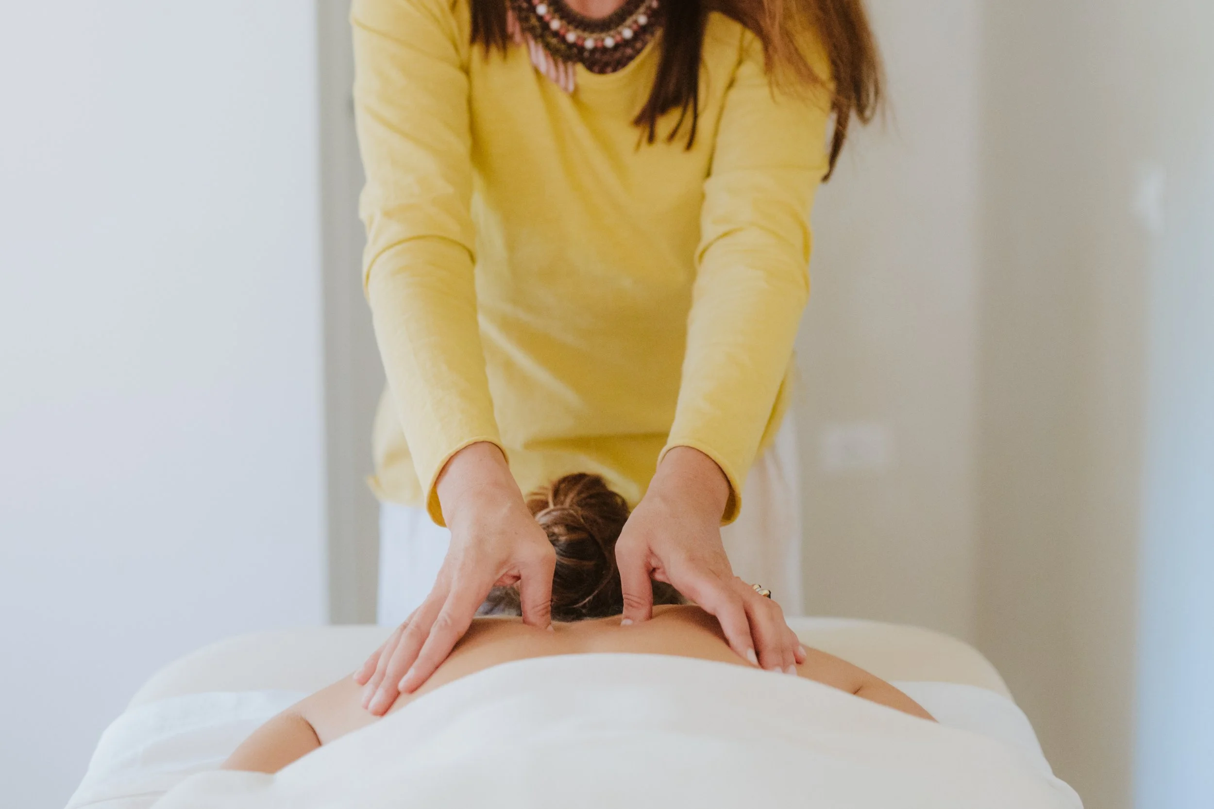 Una donna che riceve un massaggio sulla schiena, vista di schiena con le mani dell'operatrice che massaggiano.