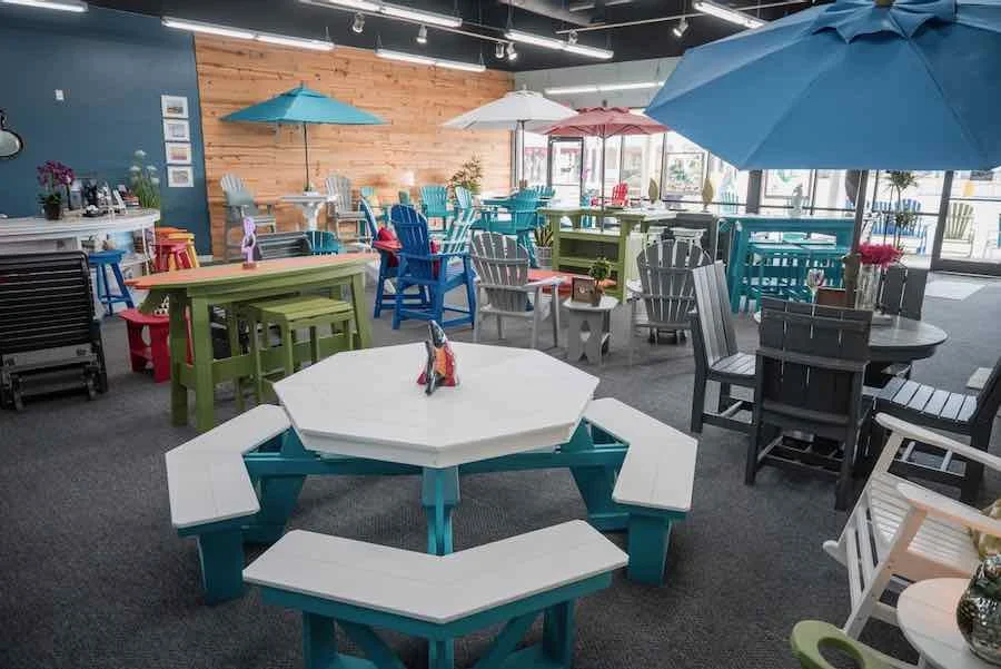 Indoor furniture display with colorful outdoor-style tables and chairs, large umbrellas, and a wooden accent wall, resembling a patio setup.