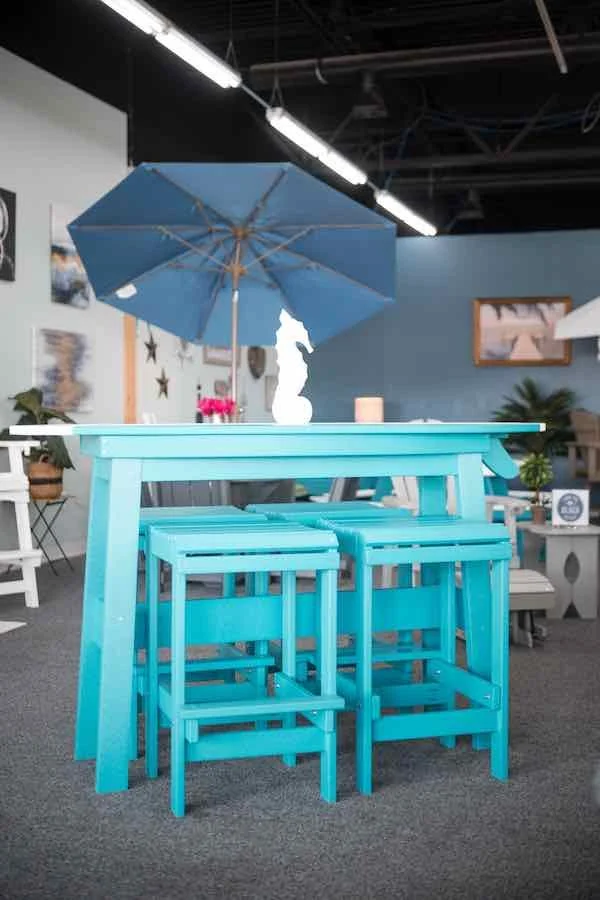 Blue outdoor table with matching stools, a large blue umbrella, and a white decorative figure on the table inside a showroom.