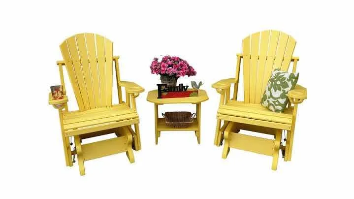 Two yellow Adirondack chairs with a small yellow side table in between, decorated with pink flowers, a small black sign that says "Family," and a green and white patterned pillow on one chair.