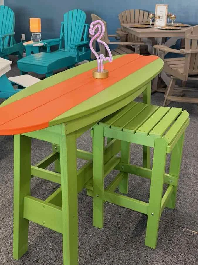 A colorful outdoor table and high chair set, with a flamingo-shaped neon light on the table, surrounded by different styles of outdoor chairs.