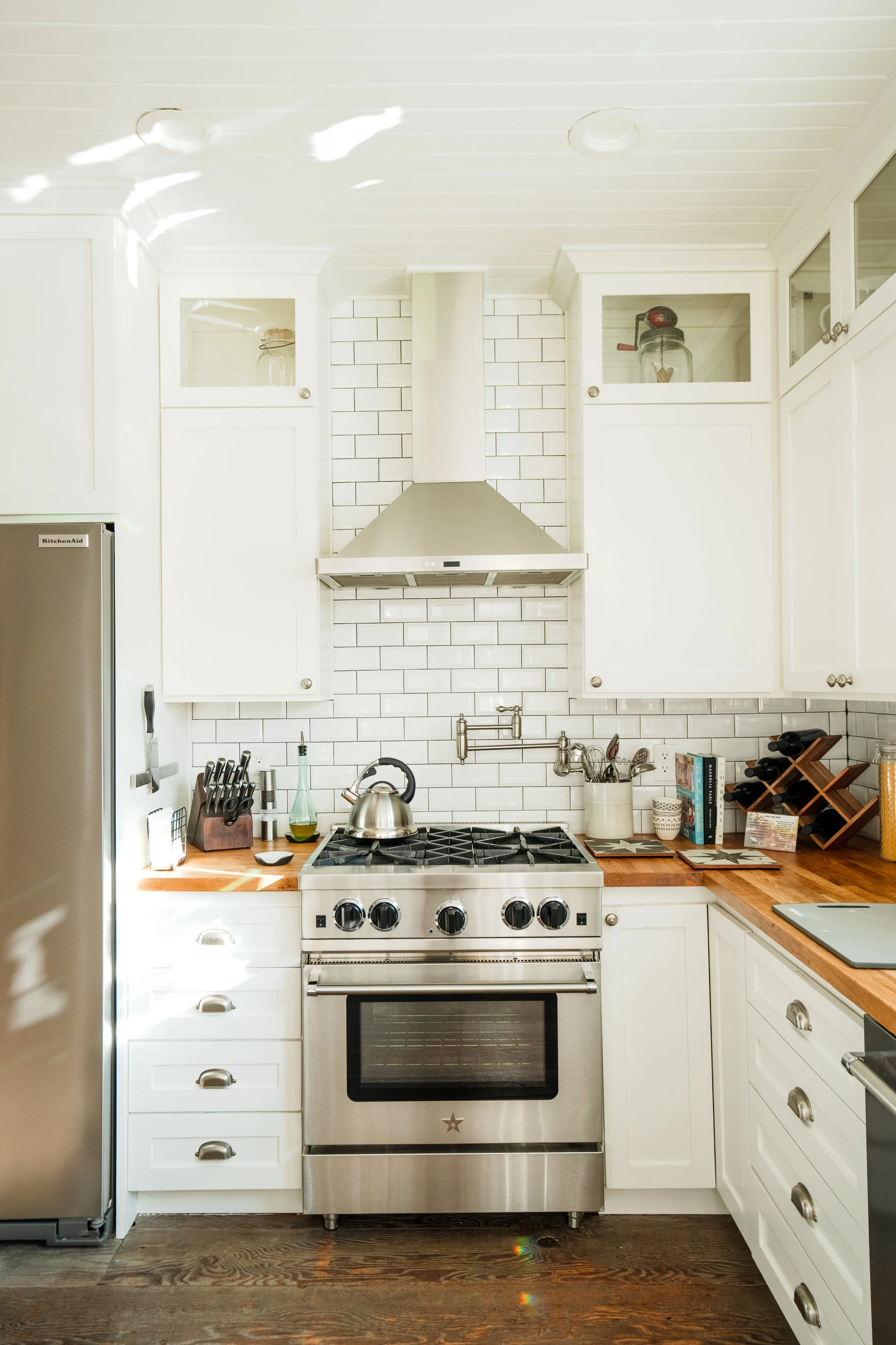 Modern kitchen with white cabinetry, stainless steel stove, wooden countertops, and white tiled backsplash.