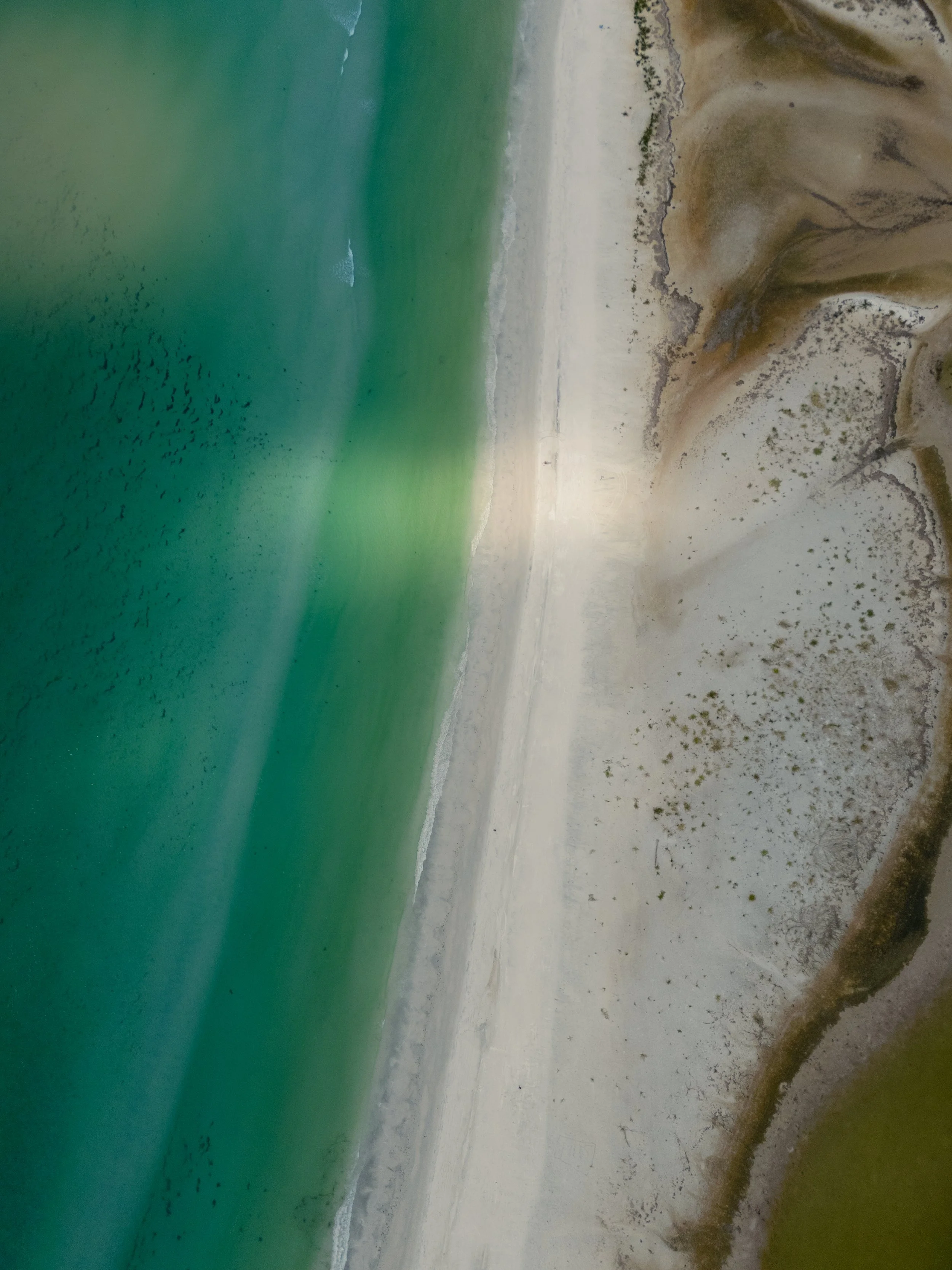 Aerial view of a coastal landscape showing the turquoise ocean, sandy beach, and rocky cliffs.
