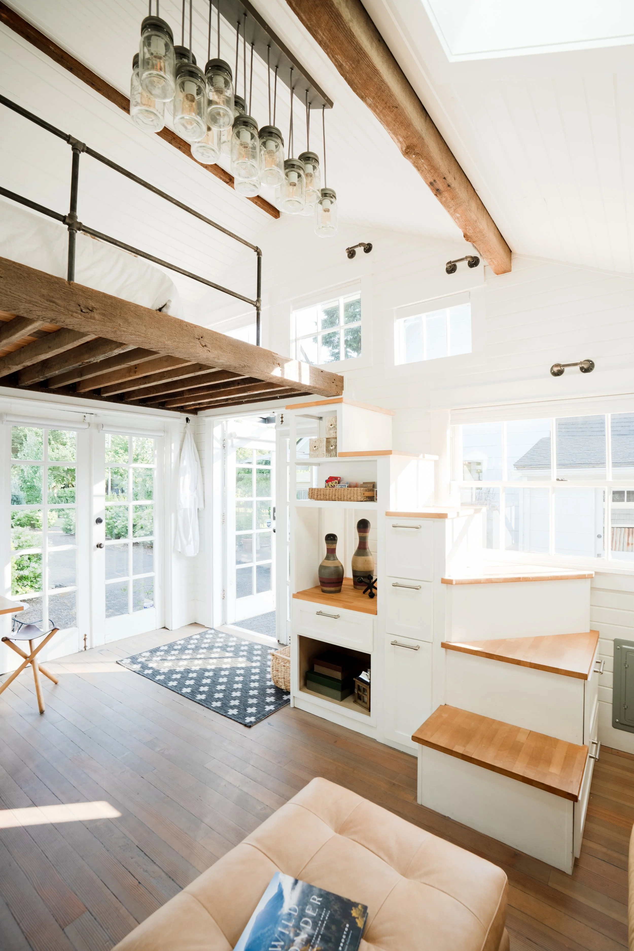 Bright living room featuring a staircase with wooden steps, large windows, and a loft area with hanging glass jar light fixture.