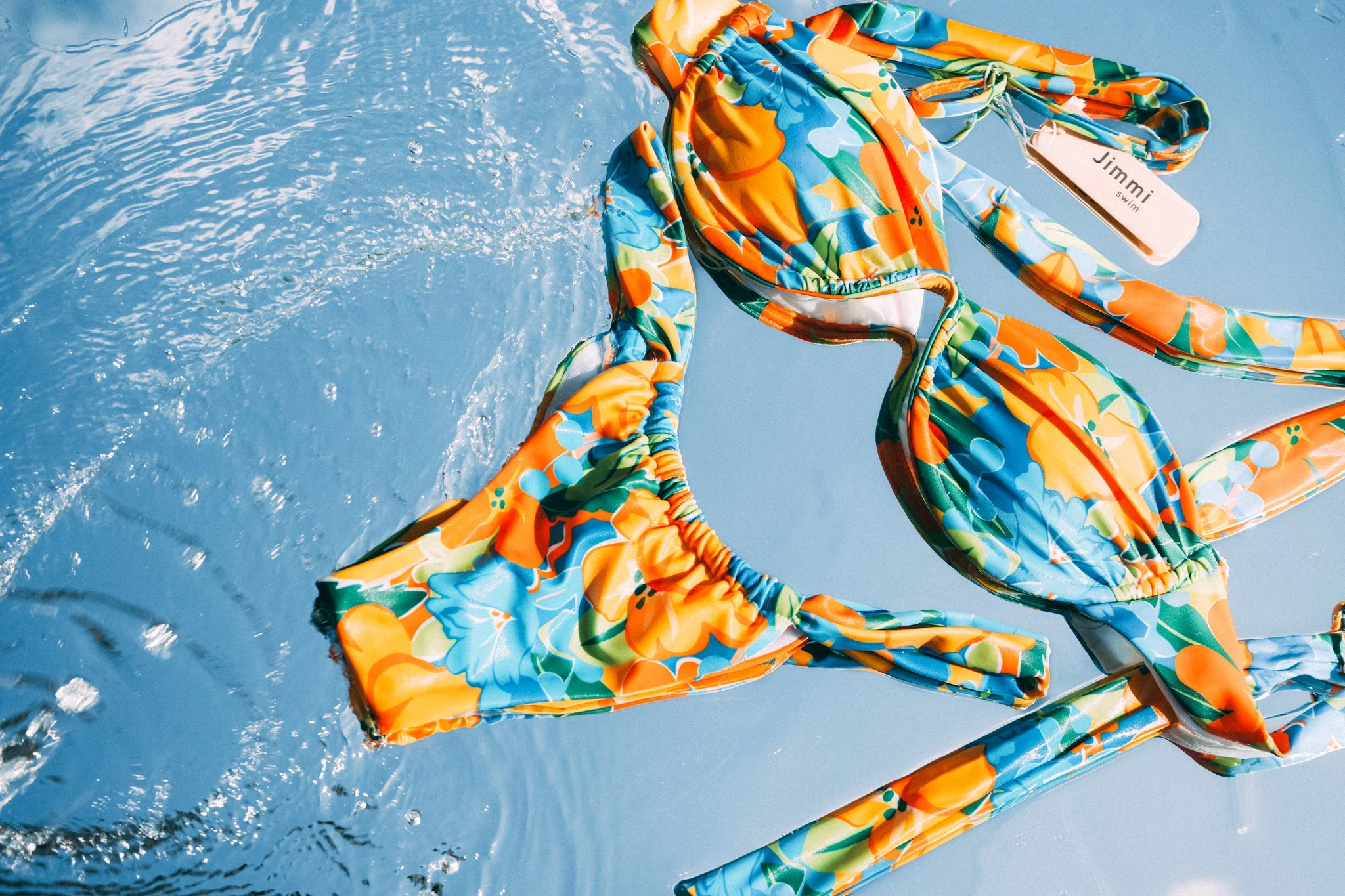 Colorful floral-patterned bikini with blue, orange, green, and white colors floating on water.