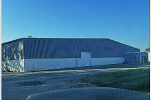 Large blue industrial warehouse building with white lower walls under a clear blue sky.