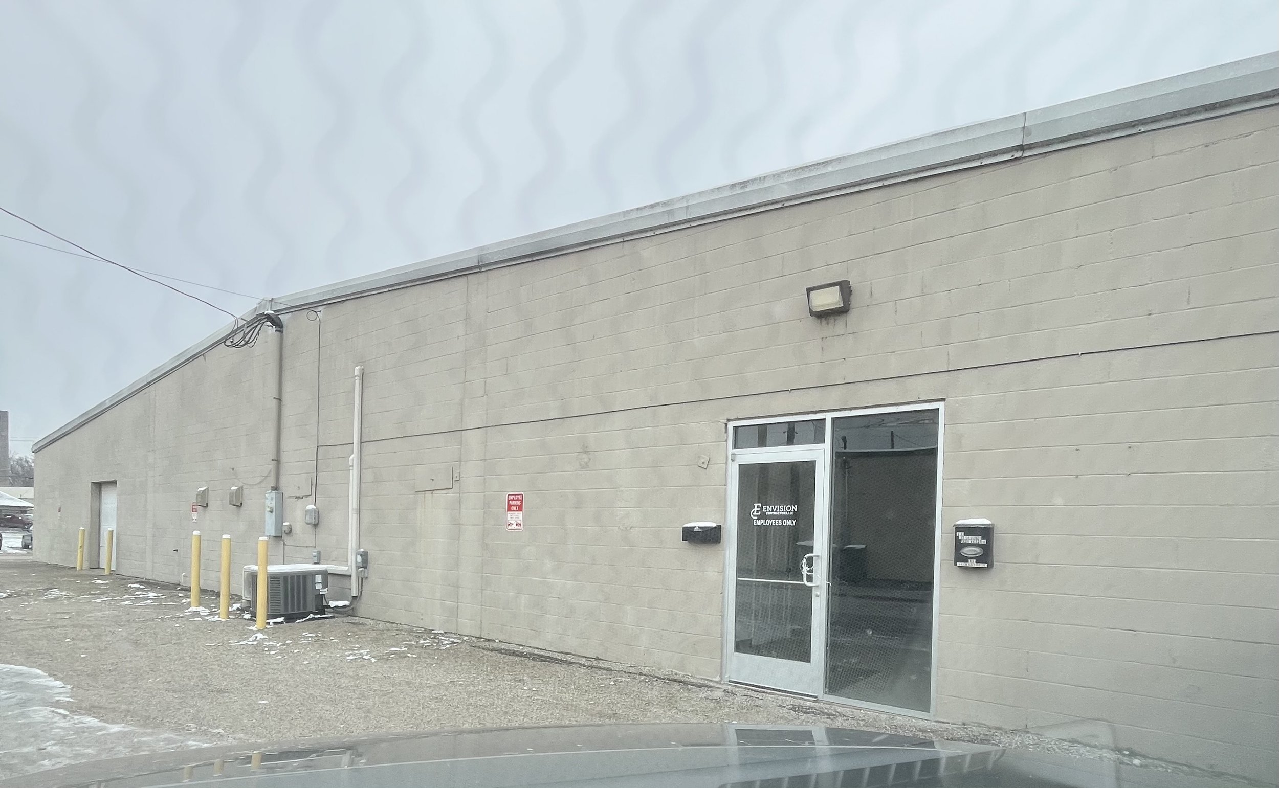 Large industrial warehouse building on a street with a utility pole and shadowed sidewalk, under a clear blue sky.