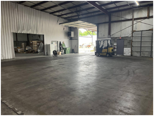 Empty warehouse with a yellow forklift and some storage containers near the back wall.