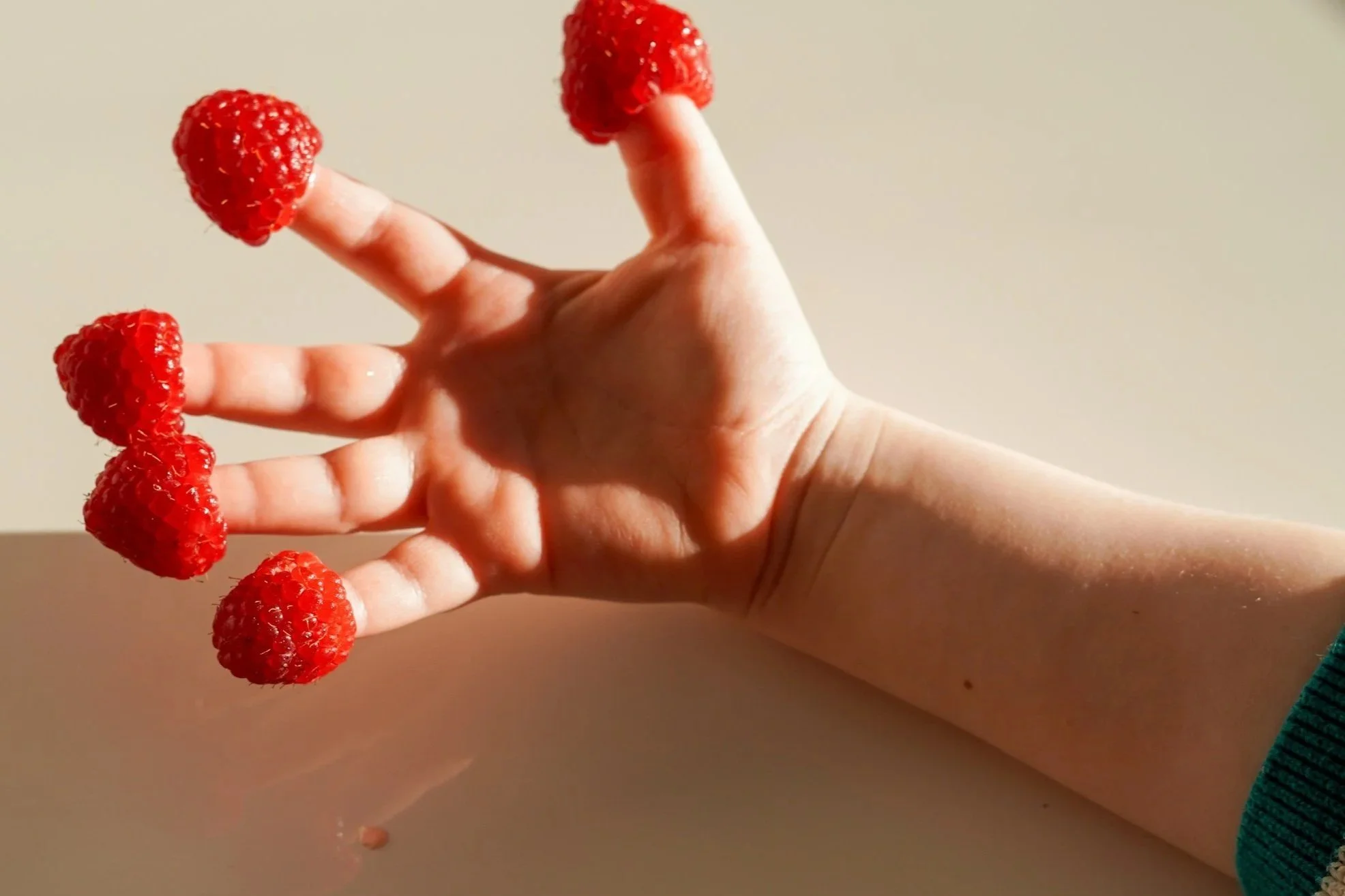 Hand with strawberries on fingers, resembling claws, on a plain background.