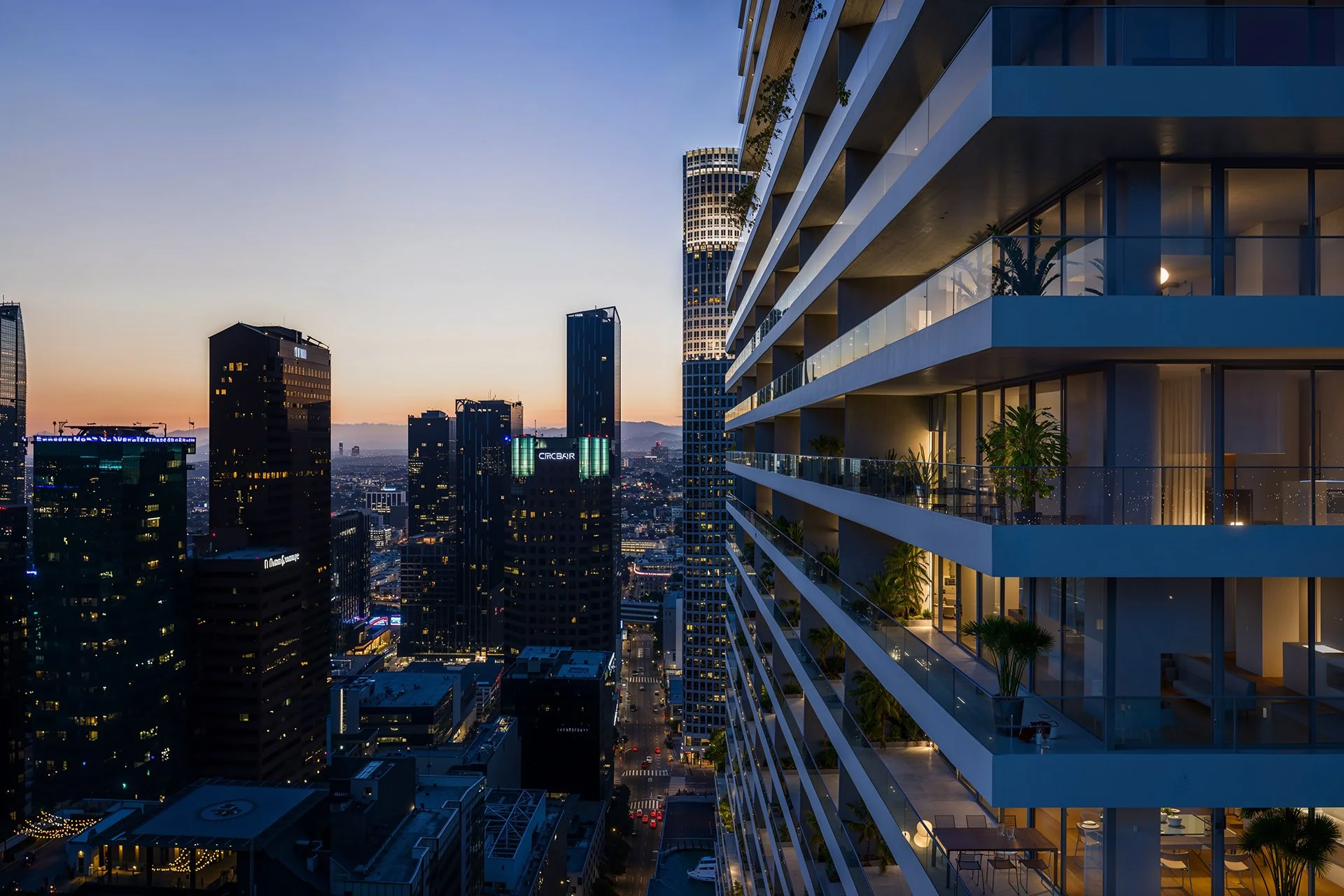 Skyline of a modern city at sunset with high-rise buildings, including a distinctive curved building, and a residential building with balconies on the right side with plants and lights