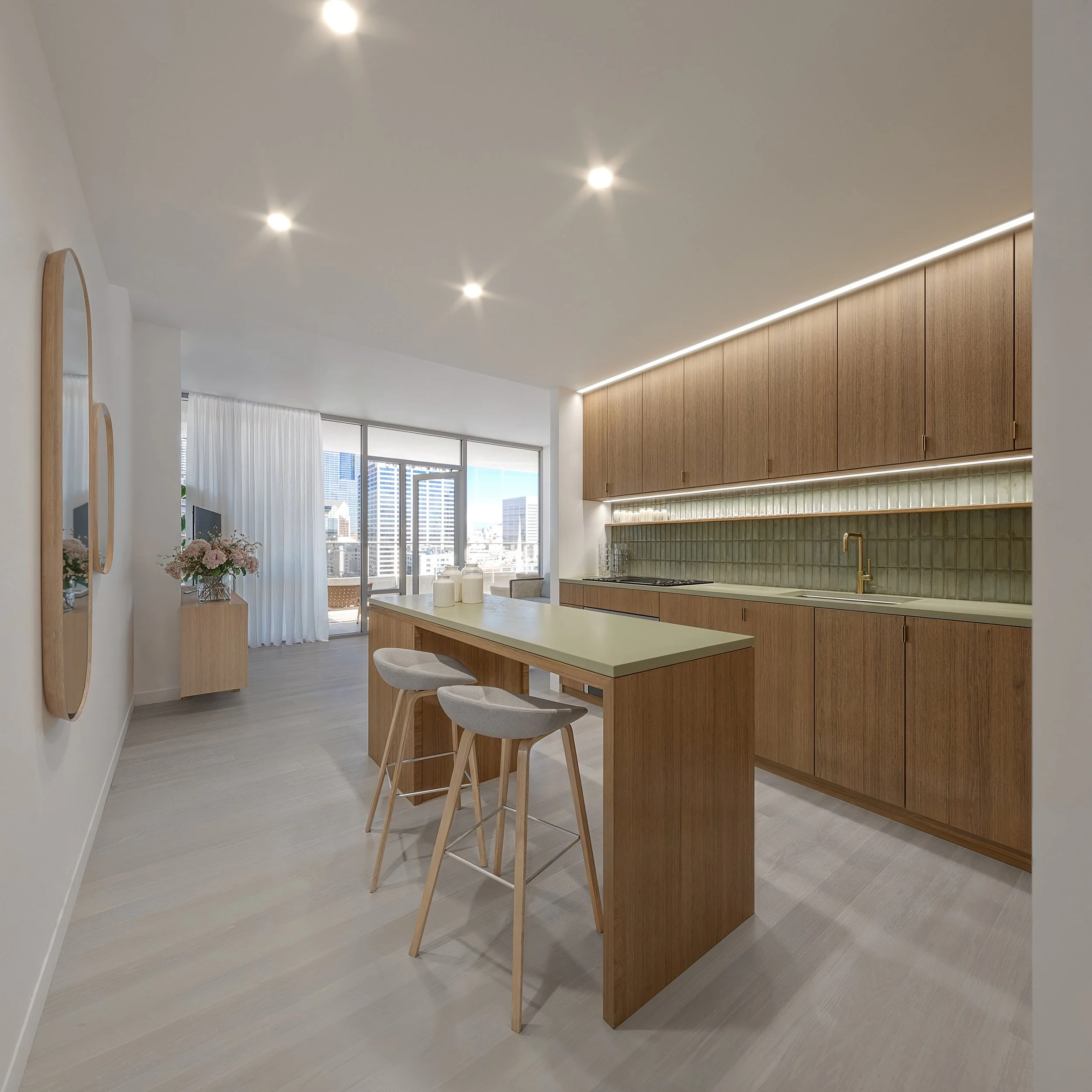 Modern kitchen with wooden cabinetry, a light-colored island with two bar stools, and a large window with city skyline view.