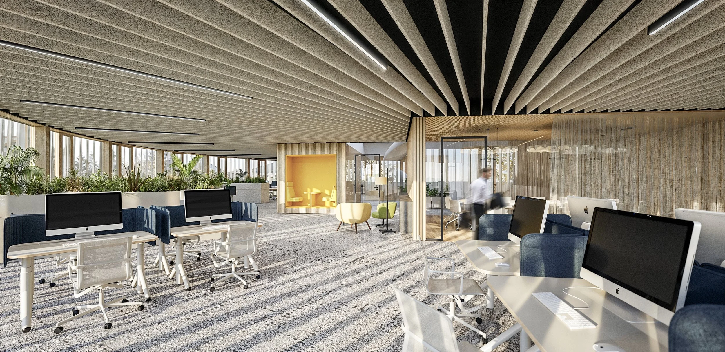 Modern office space with multiple desktop computers, comfortable chairs, and large windows with natural light. Includes a small seating area with armchairs and plants along the windows.