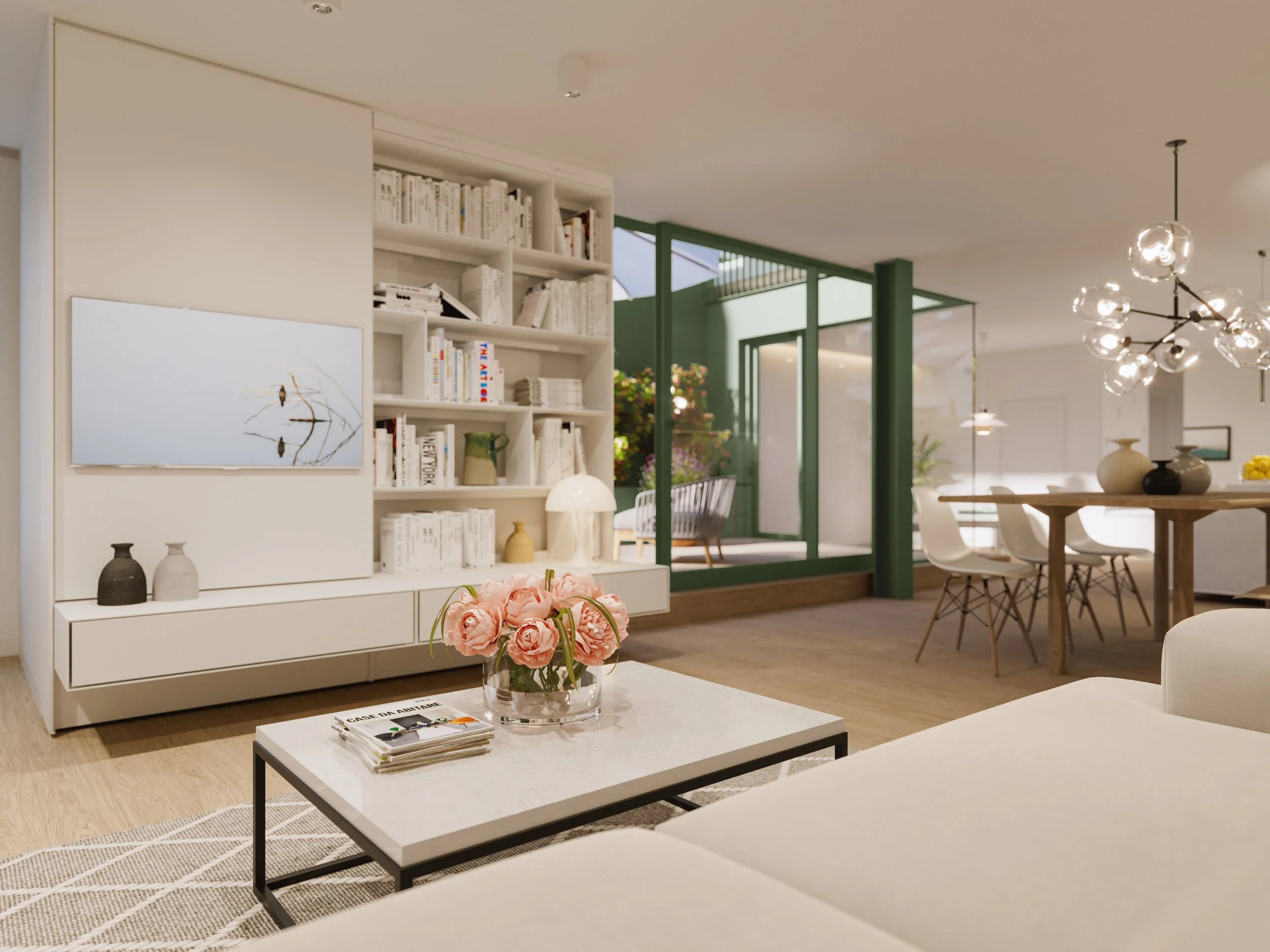 Modern living room with white shelving unit, pink roses in a glass vase on a coffee table, white couch, dining table with white chairs, and large windows with green framing letting in natural light.