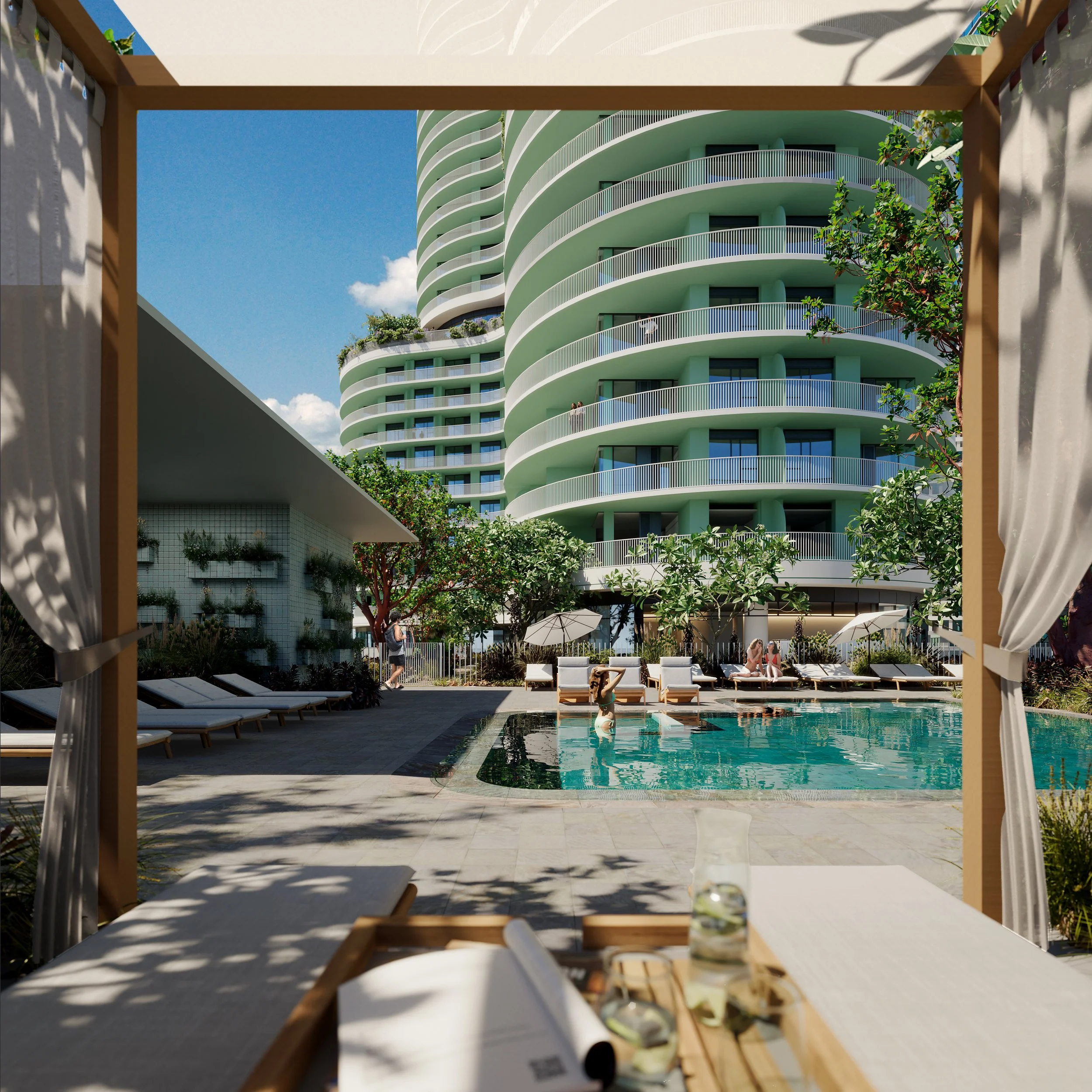 View of a luxurious pool area at a modern high-rise residential building, with lounge chairs, umbrellas, trees, and people enjoying the outdoor space under a bright blue sky.
