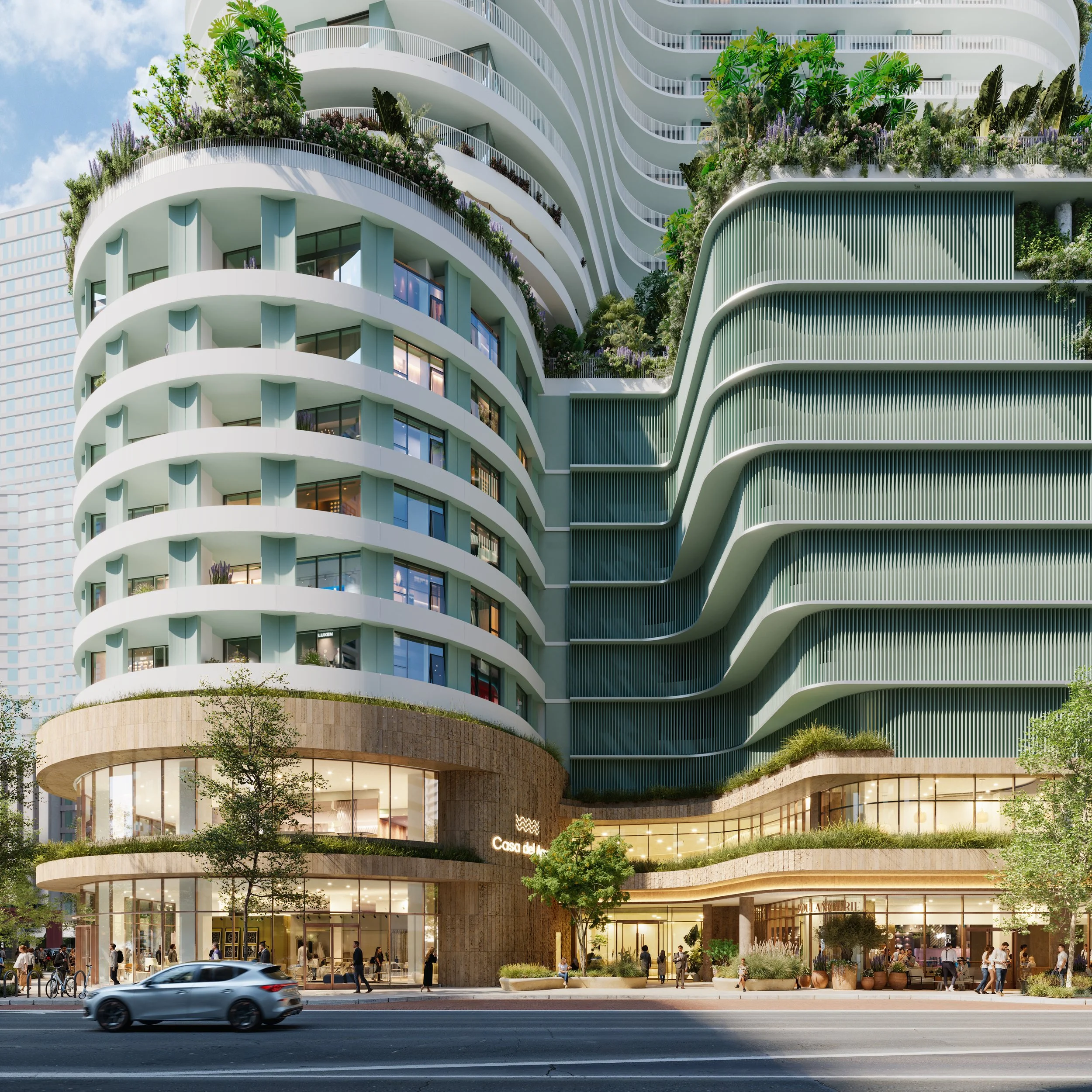 A modern multi-story building with curved balconies and greenery on upper levels, ground-floor retail shops, and a busy sidewalk with pedestrians and parked bicycles.