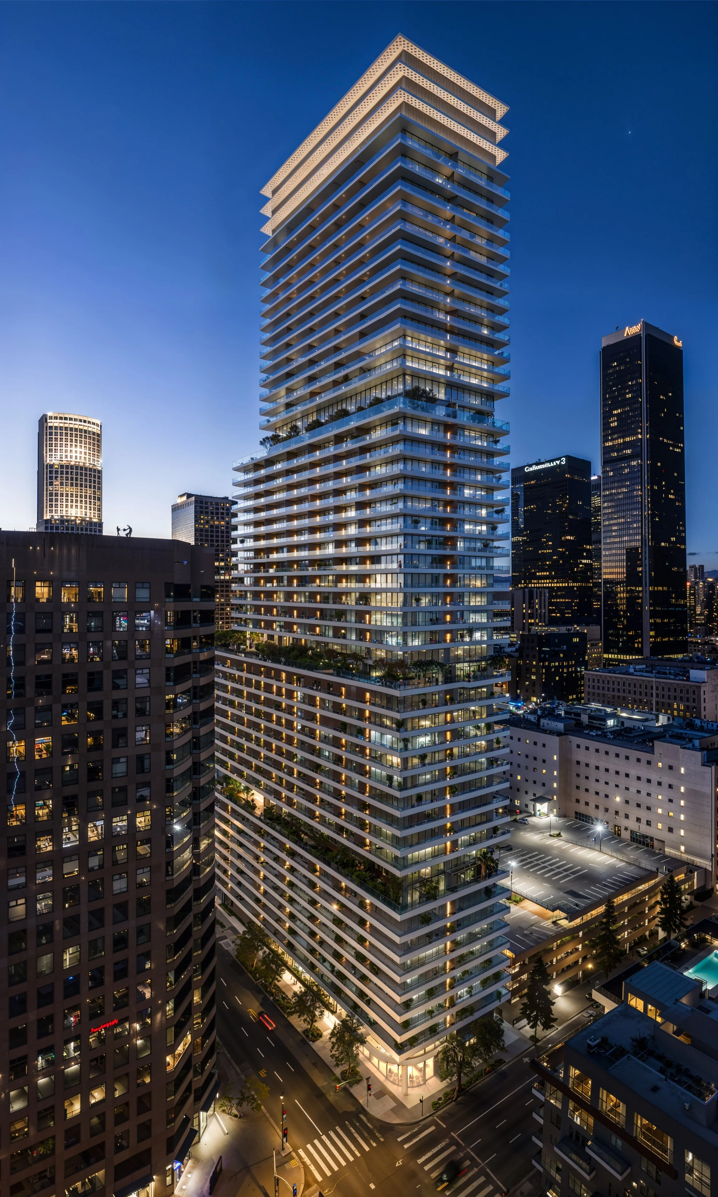 Nighttime cityscape featuring a tall modern residential building with multiple balconies and glass facade, surrounded by other high-rise buildings in a metropolitan downtown area.