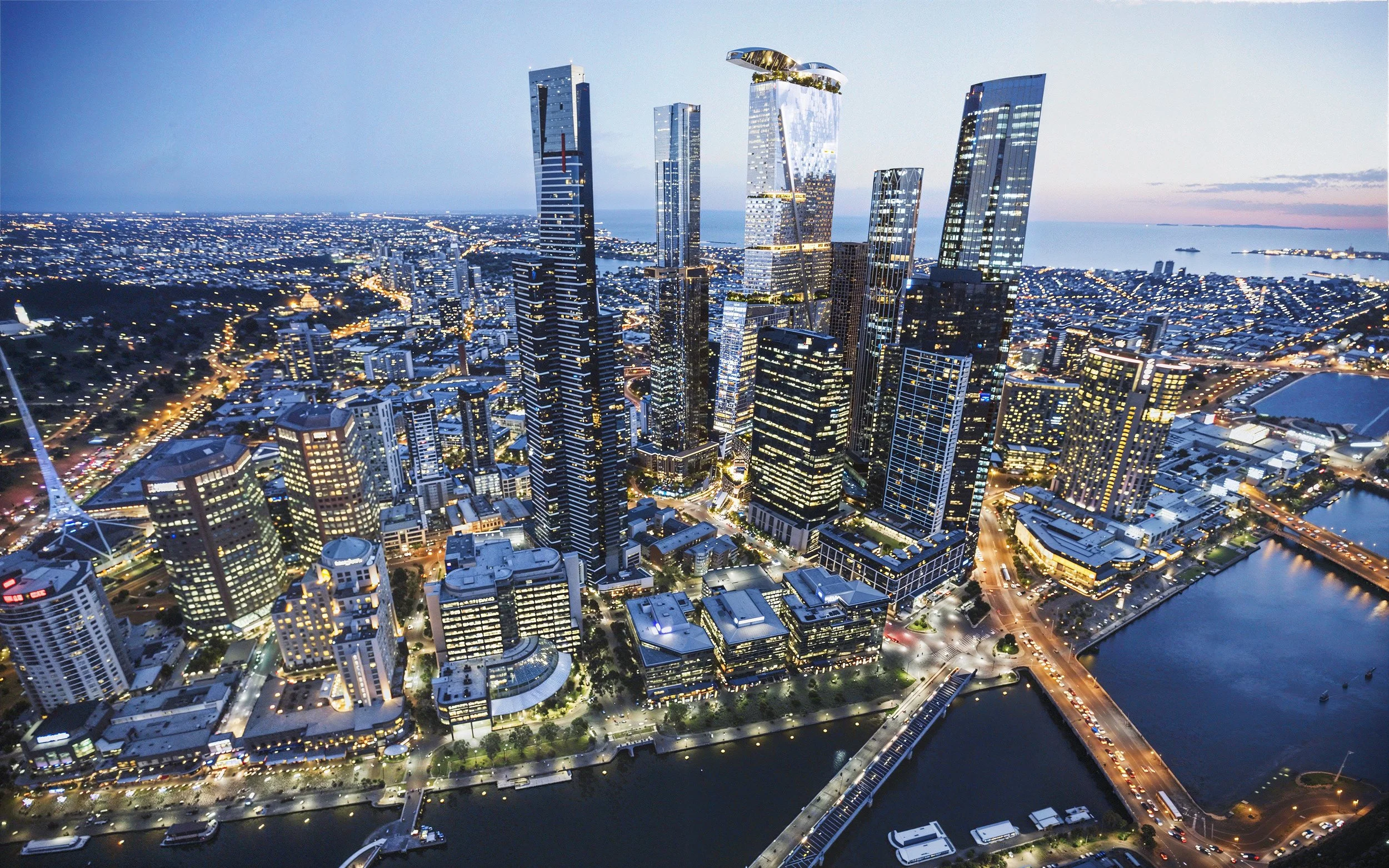 Aerial view of a city skyline at dusk with illuminated skyscrapers, water bodies, and a network of streets.